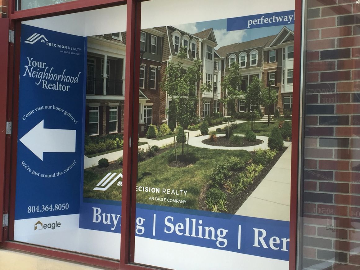 A real estate office window displaying a photo of townhomes and advertising buying, selling, and rental services.