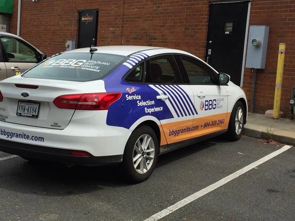 A white car branded with BBG, featuring blue and orange decals, parked in a parking lot next to a brick building.