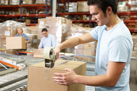 A man is taping a cardboard box in a warehouse.