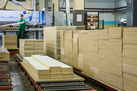 A man is standing next to a conveyor belt filled with stacks of wood in a factory.