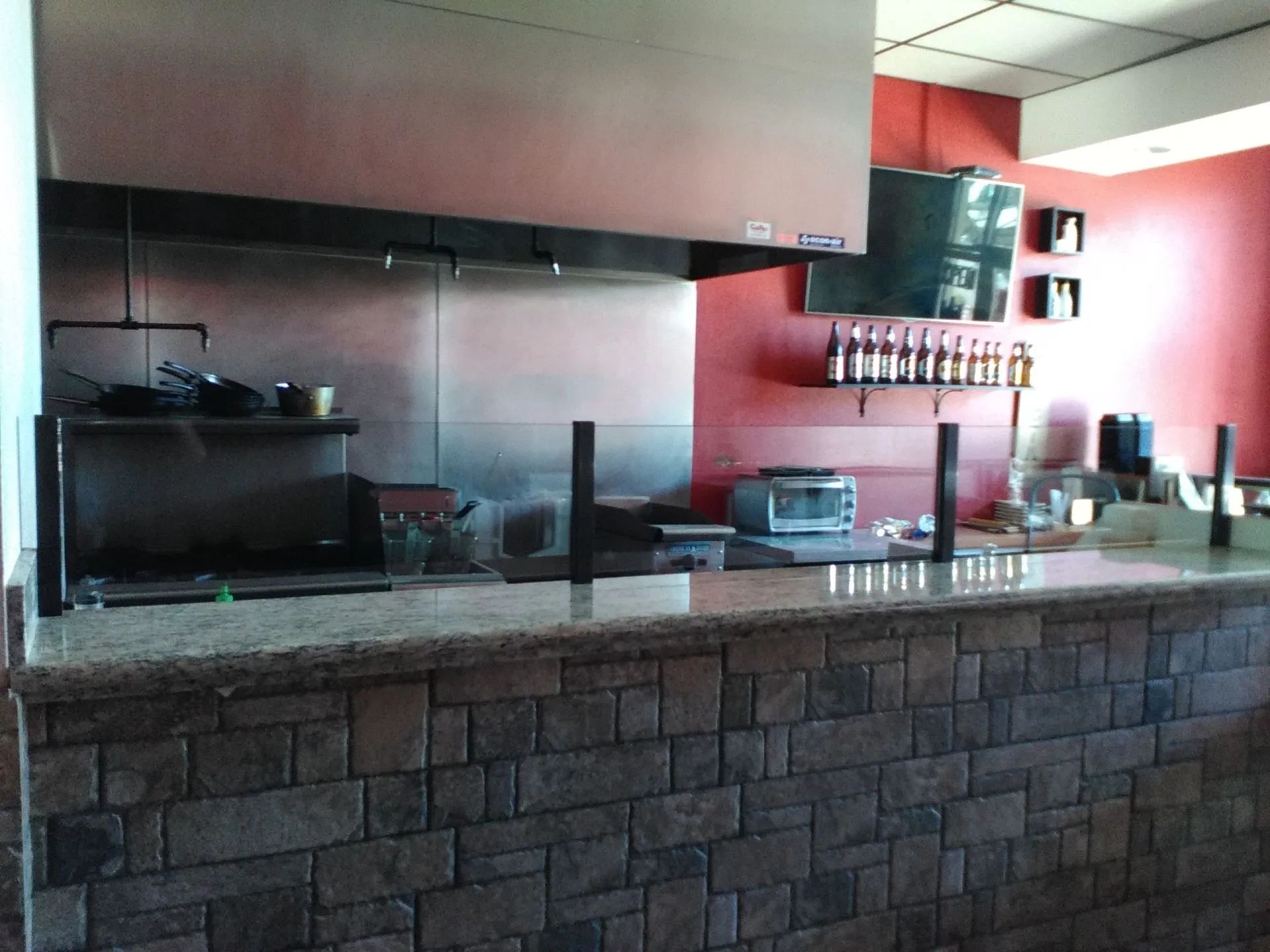 Empty restaurant counter with stone facade, stainless steel kitchen pass, and red wall shelves.
