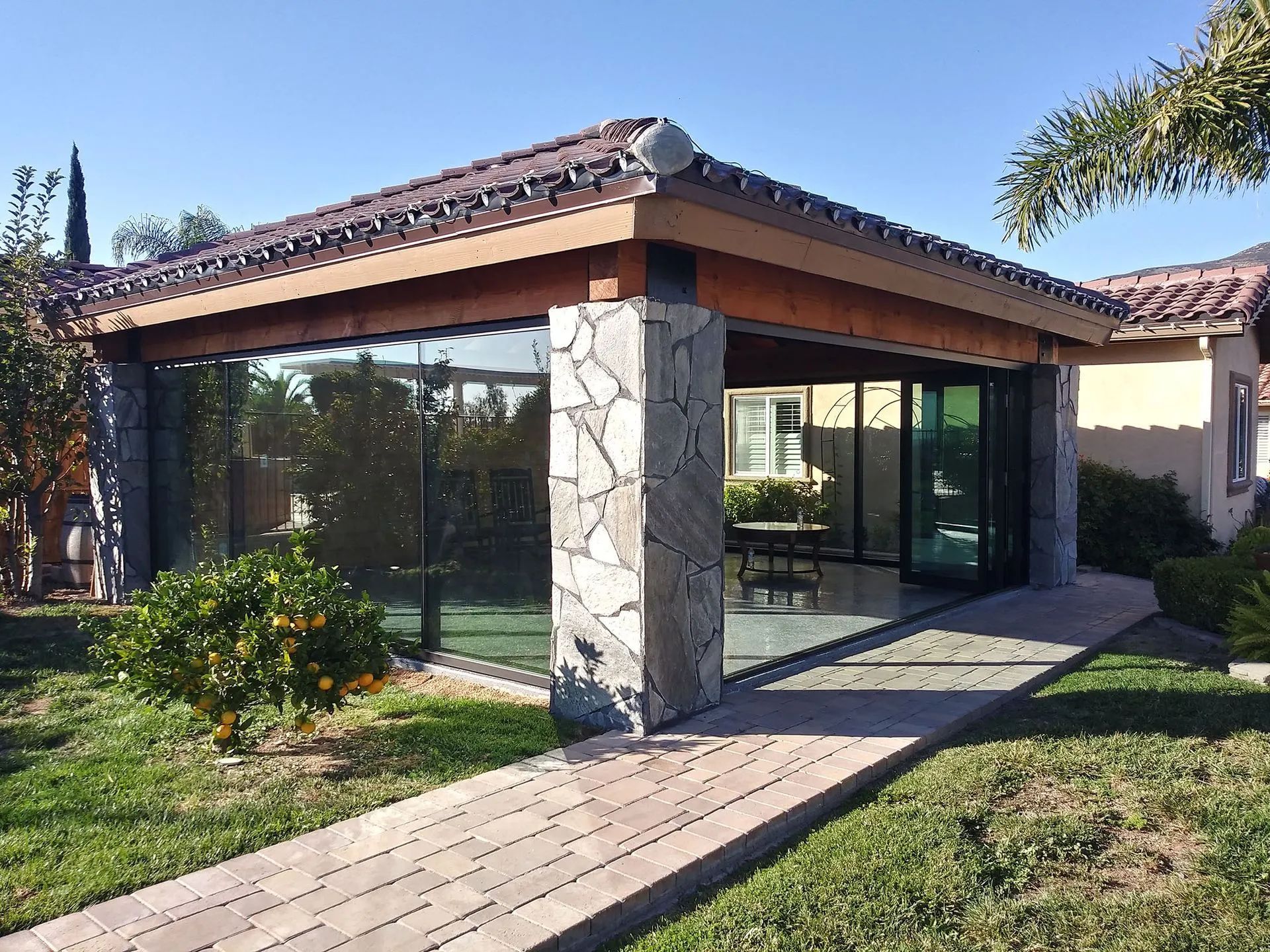 Modern building with stone columns, glass walls, and a tiled roof beside a walkway and lawn