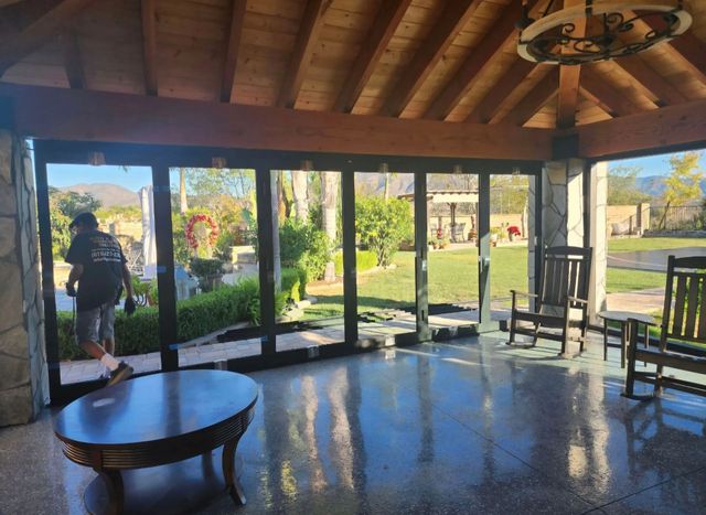 Covered patio with large glass doors, round table, and a person standing by the garden outside.