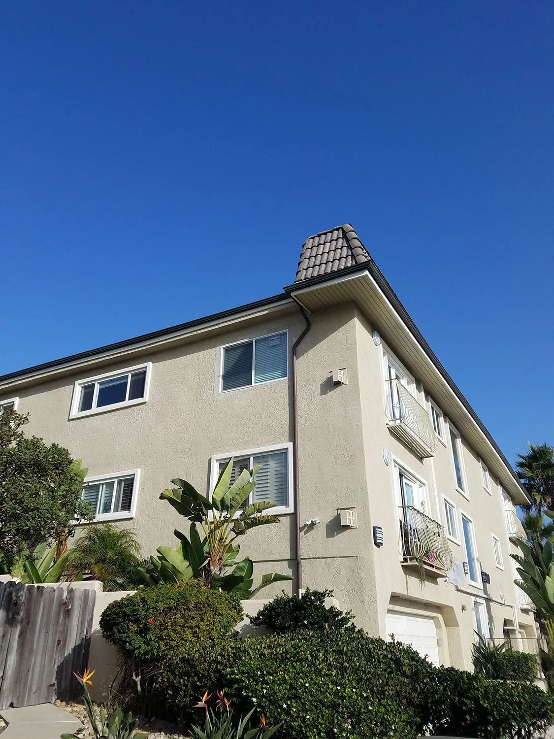 Two-story beige house with blue windows, viewed from below against a clear blue sky.