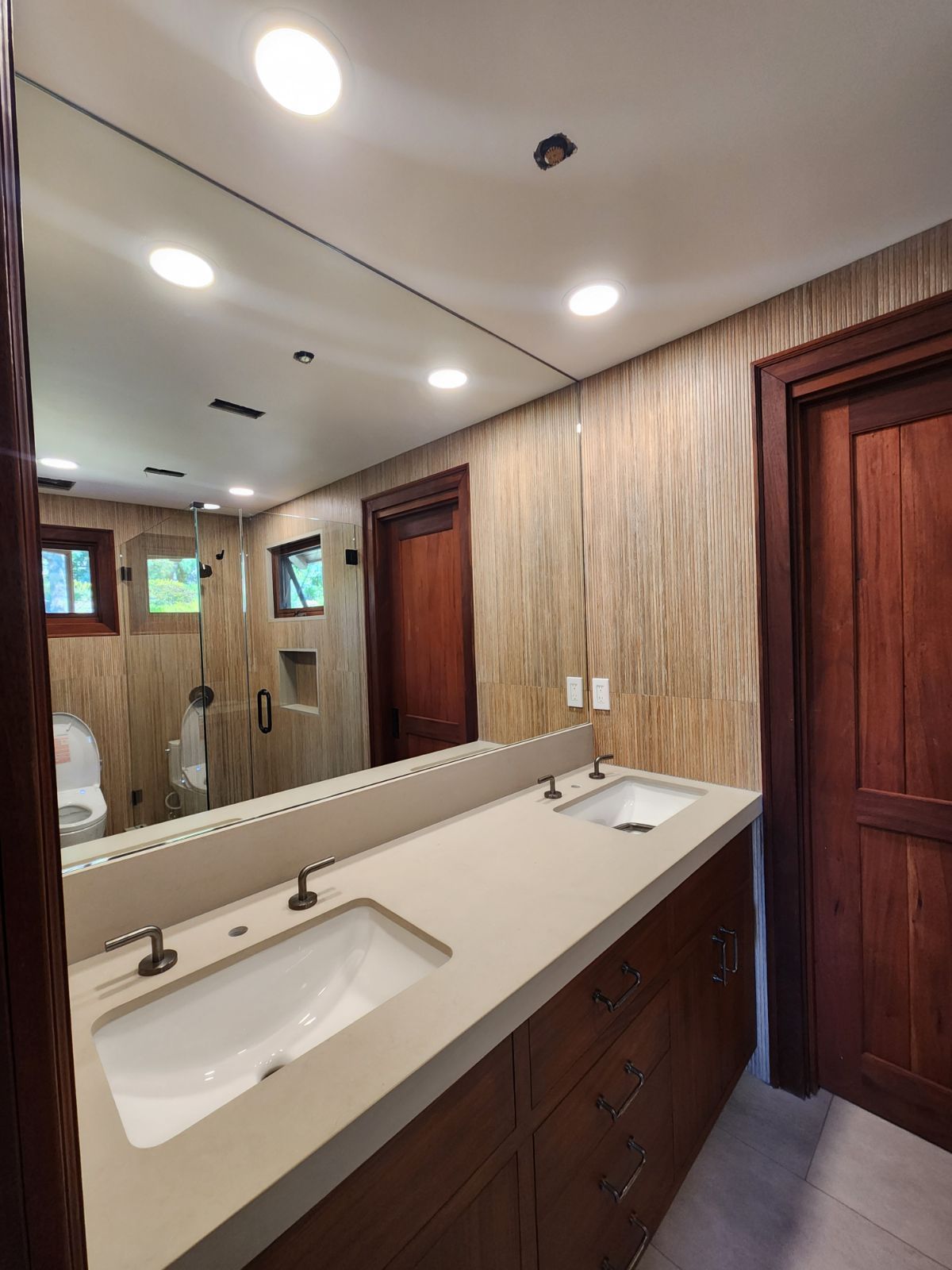 Modern bathroom with double sinks, large mirror, wood-paneled walls, and recessed ceiling lights