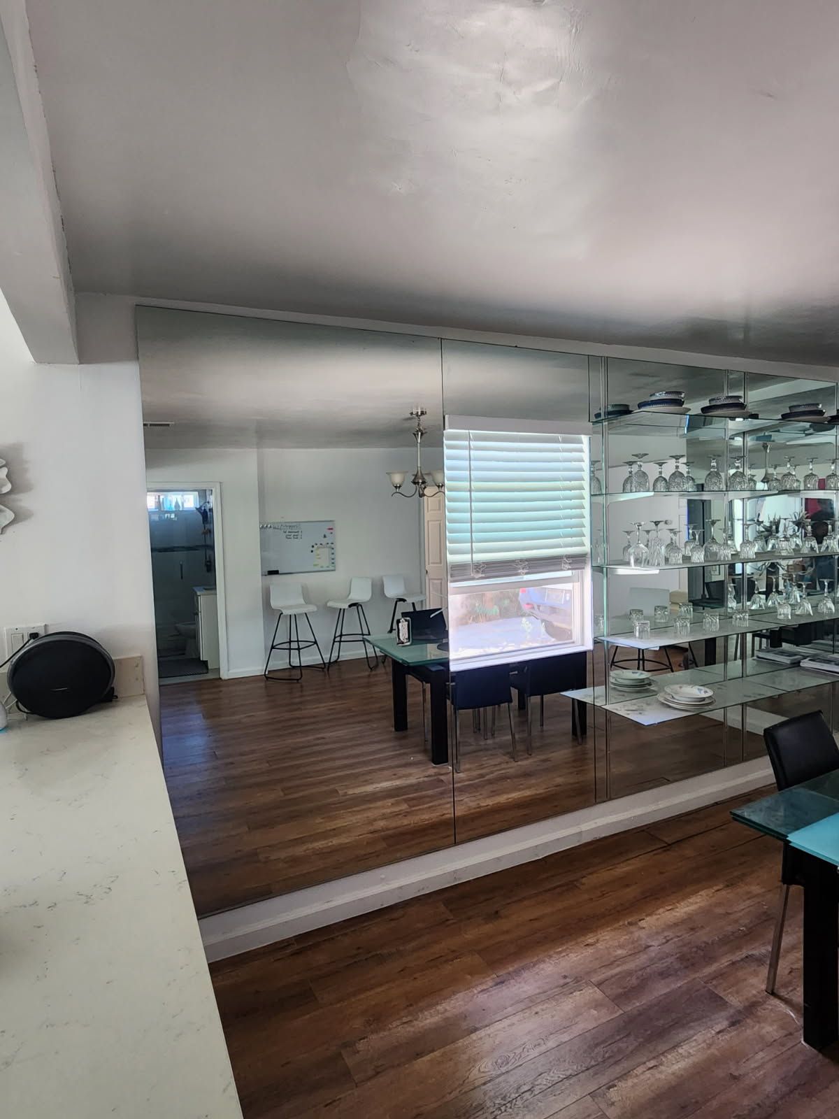 Modern living room with wall mirror, dark wood floor, white walls, and glass shelving by a window