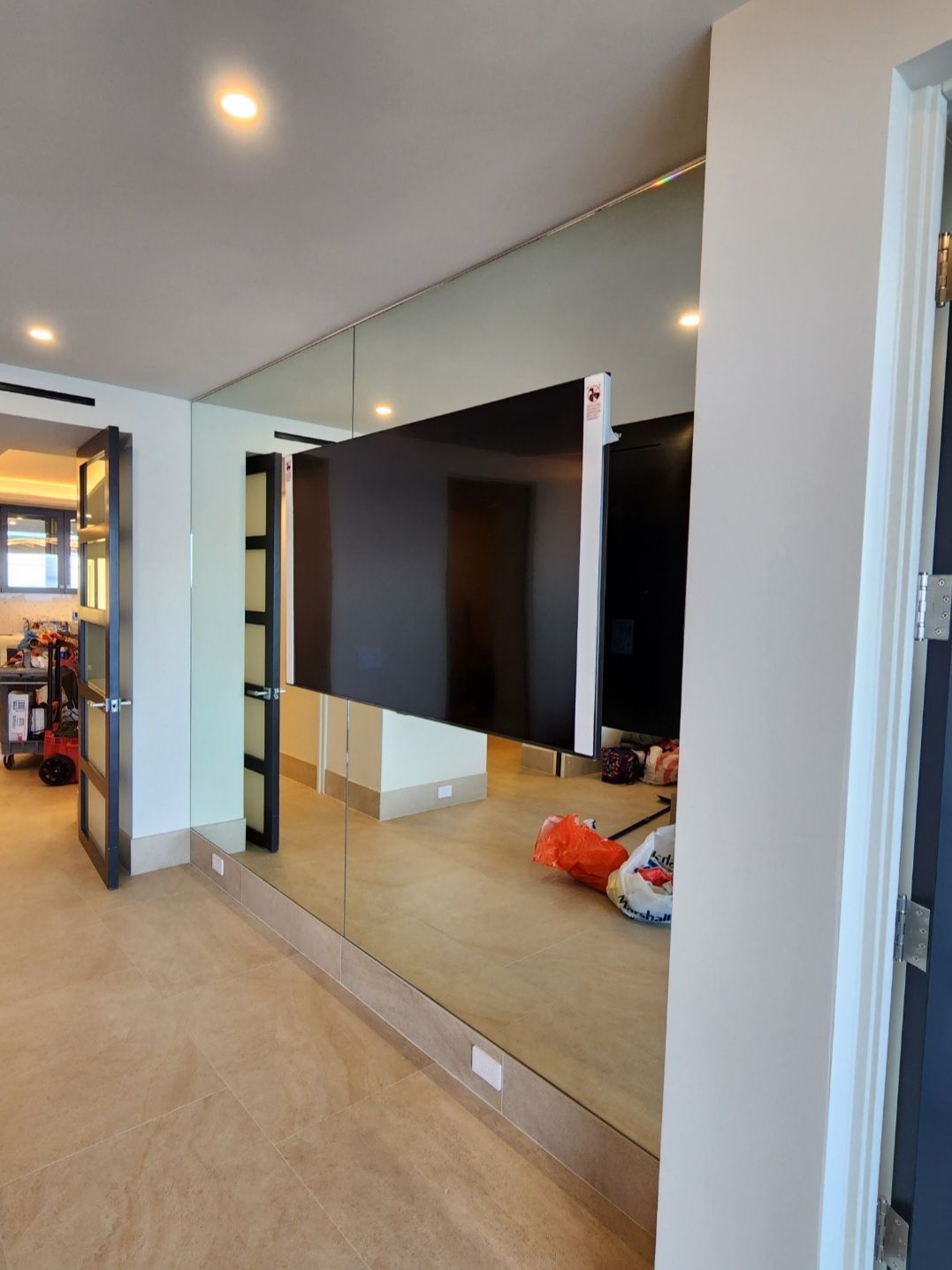 Large wall-mounted TV beside a mirrored wall in a carpeted living room hallway