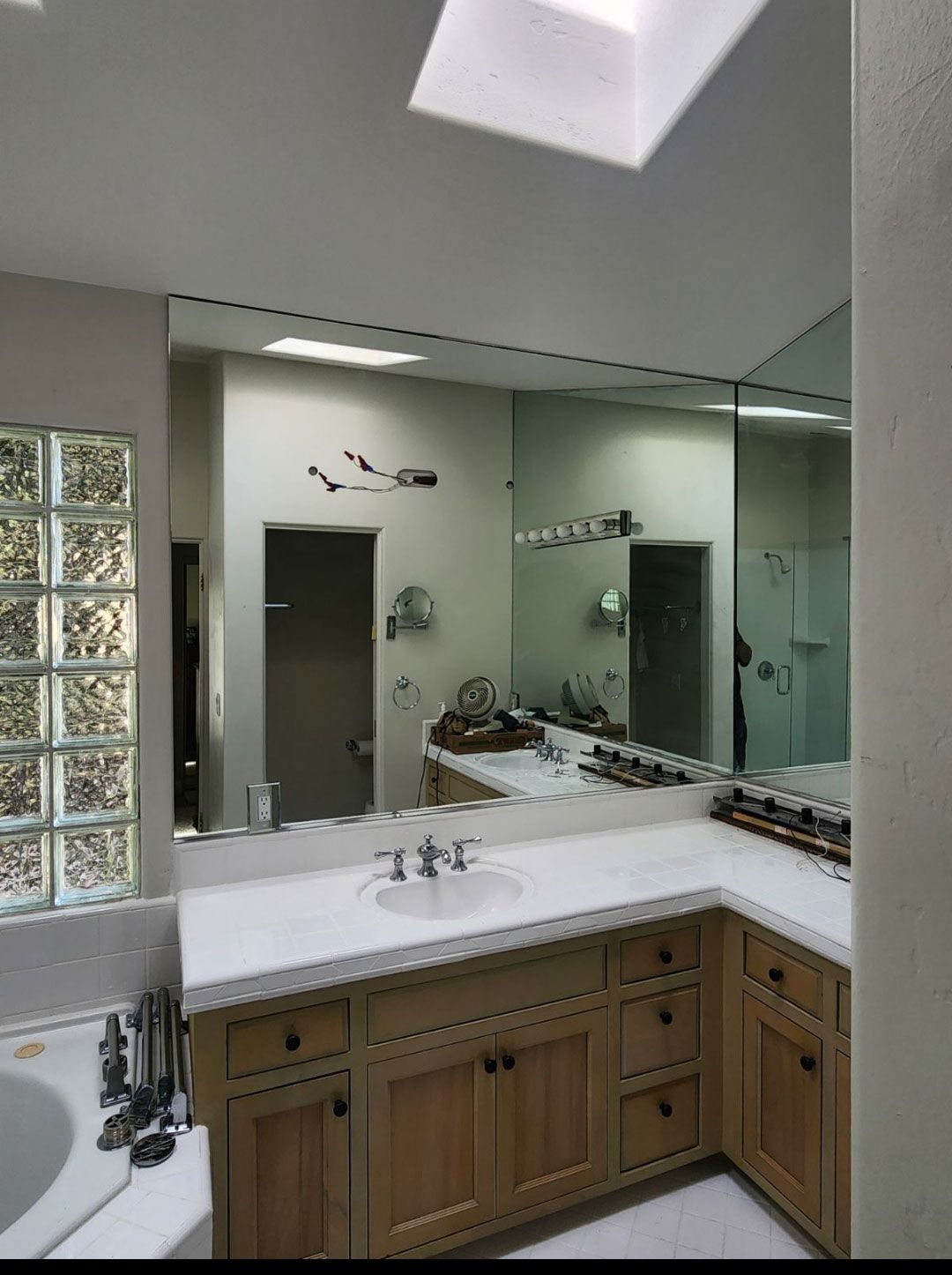 Bright bathroom vanity with white countertop, wood cabinets, large mirror, and glass block window.