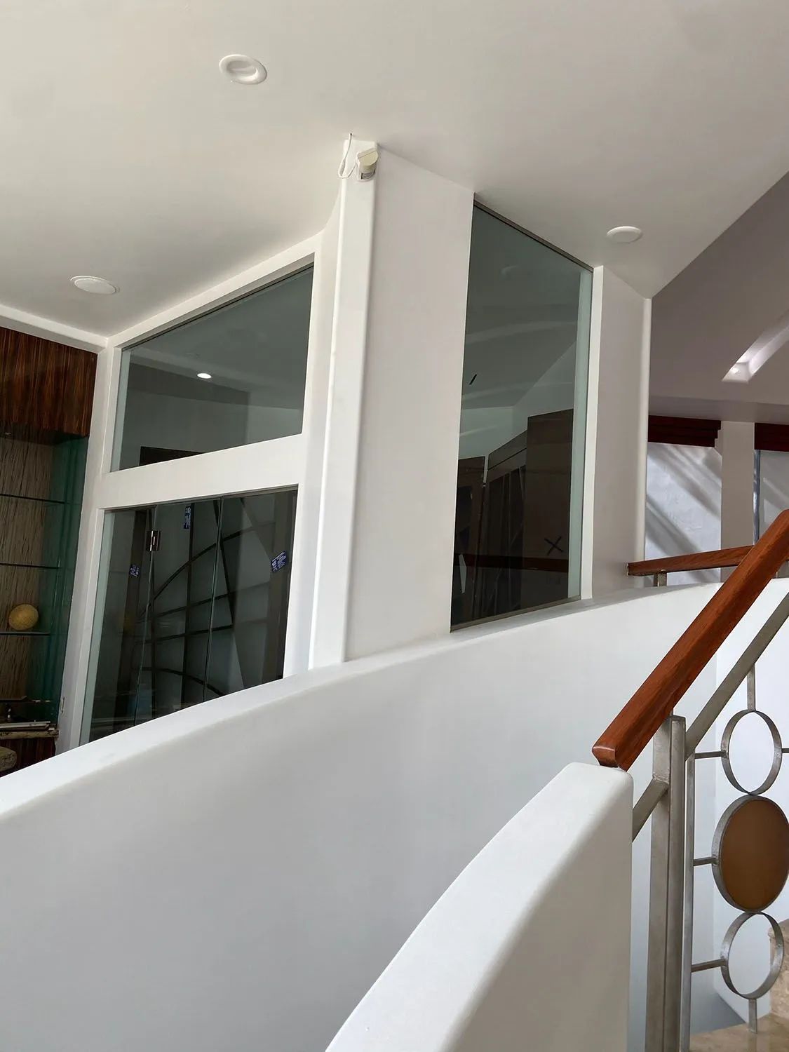 Modern staircase with white walls, glass railing, and wood handrail in a bright interior.