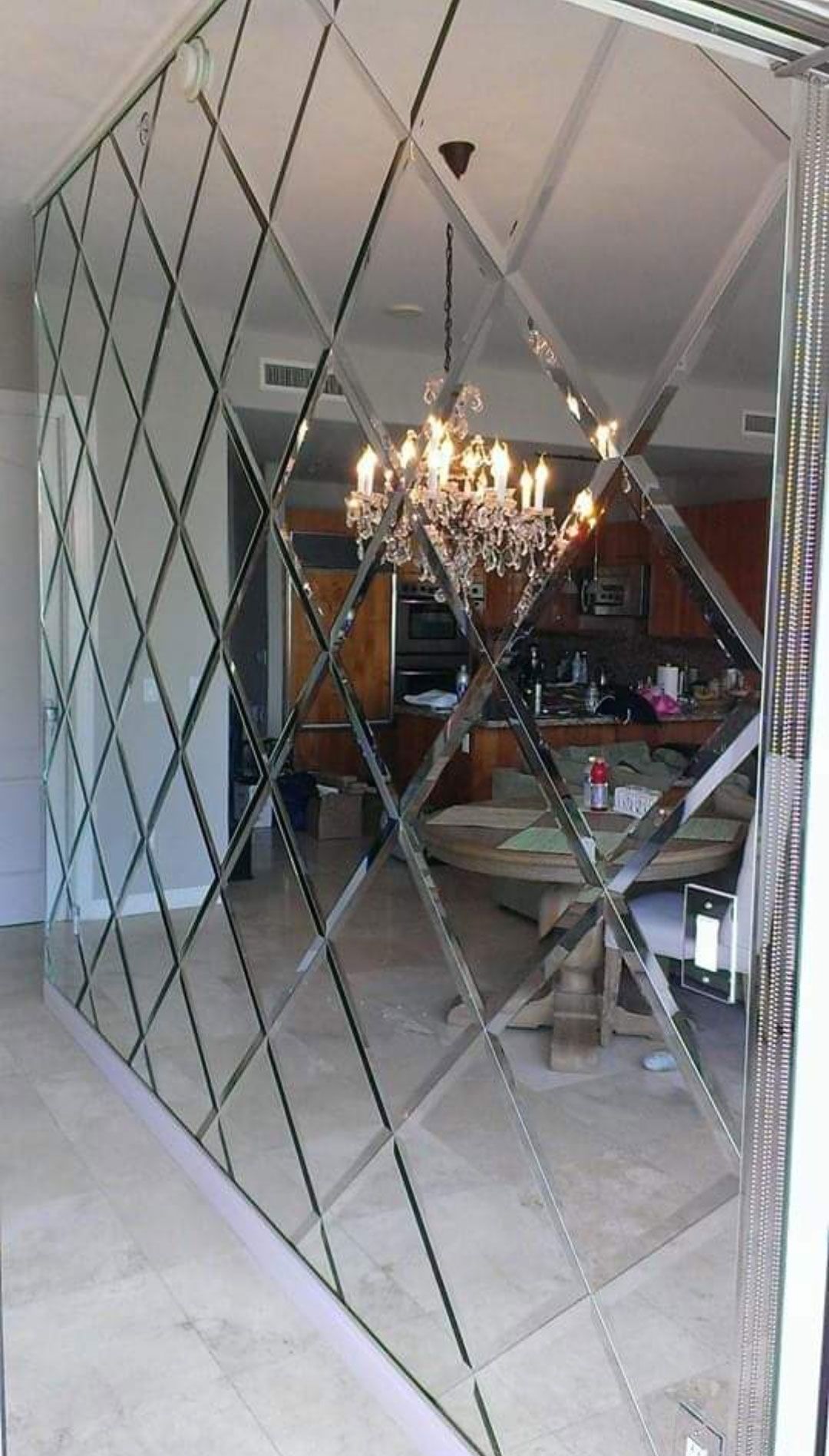 Diamond-pattern mirrored wall reflecting a dining room with a chandelier and staircase