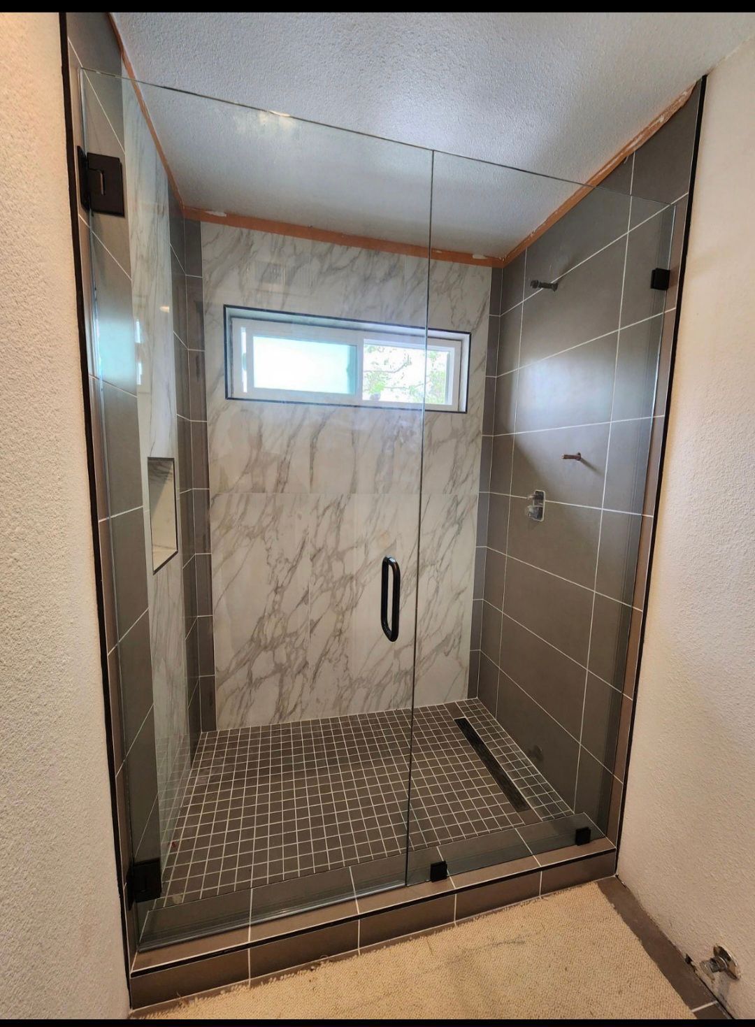 Glass shower stall with tiled walls, pebble floor, and small frosted window