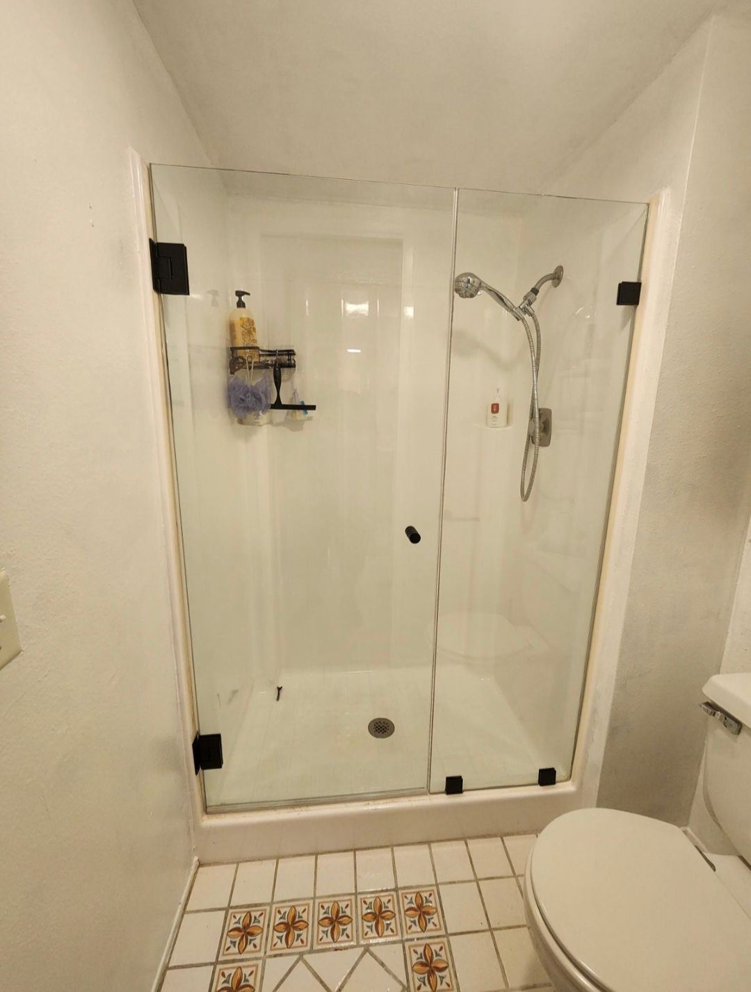 Small bathroom with glass shower enclosure, tiled floor, and toilet in foreground.