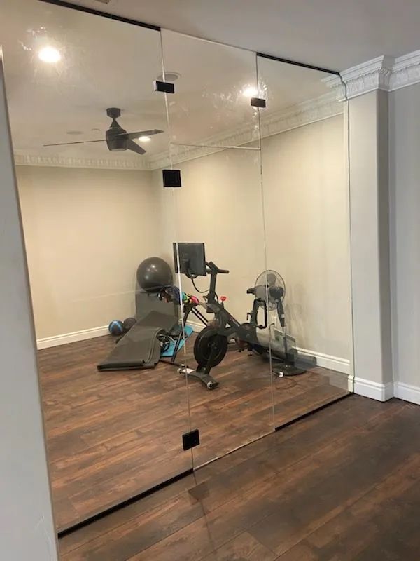 Home gym with mirrored wall, exercise bike, fan, and wood floors