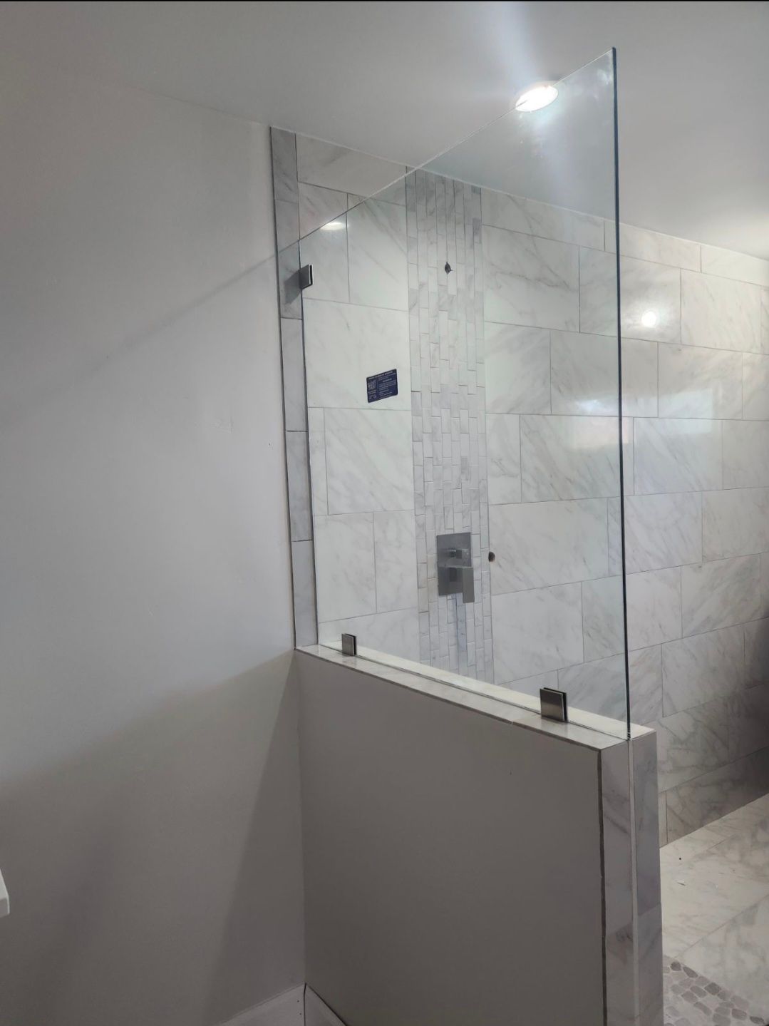 Shower enclosure with clear glass panel and marble-tiled bathroom wall