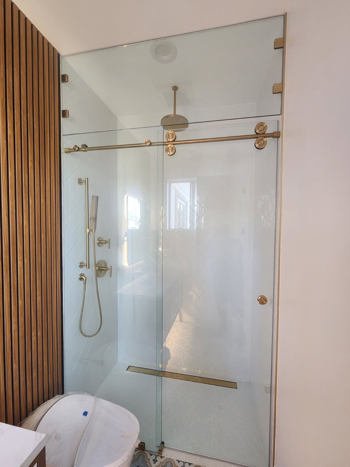 Glass walk-in shower with brass hardware and a white toilet in a bright bathroom