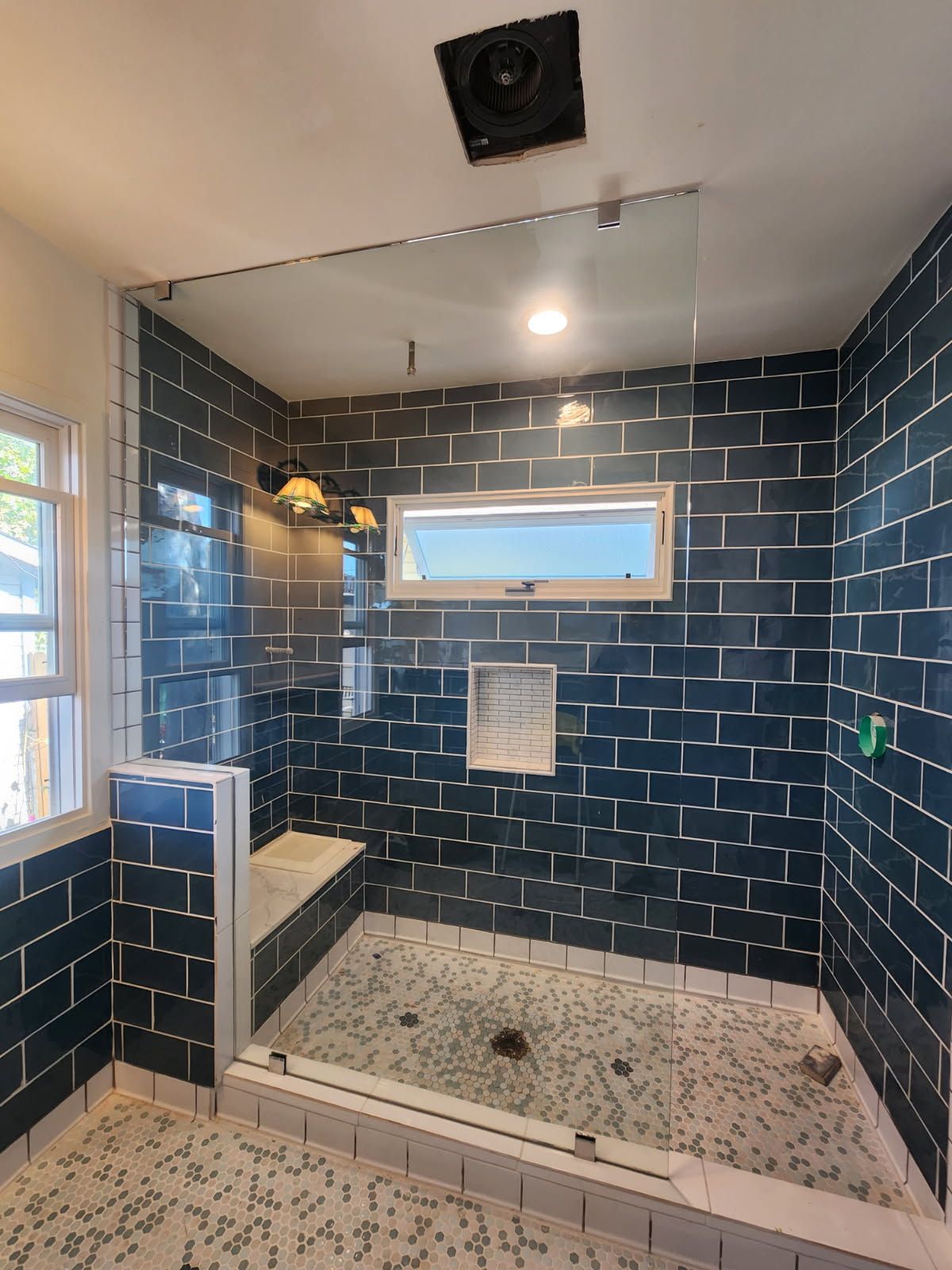 Blue-tiled shower with glass partition, built-in bench, and windows in a bathroom.