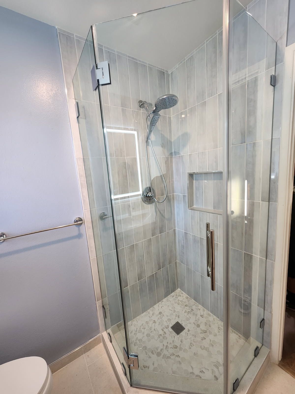 Glass shower enclosure with tiled walls and a showerhead in a small bathroom