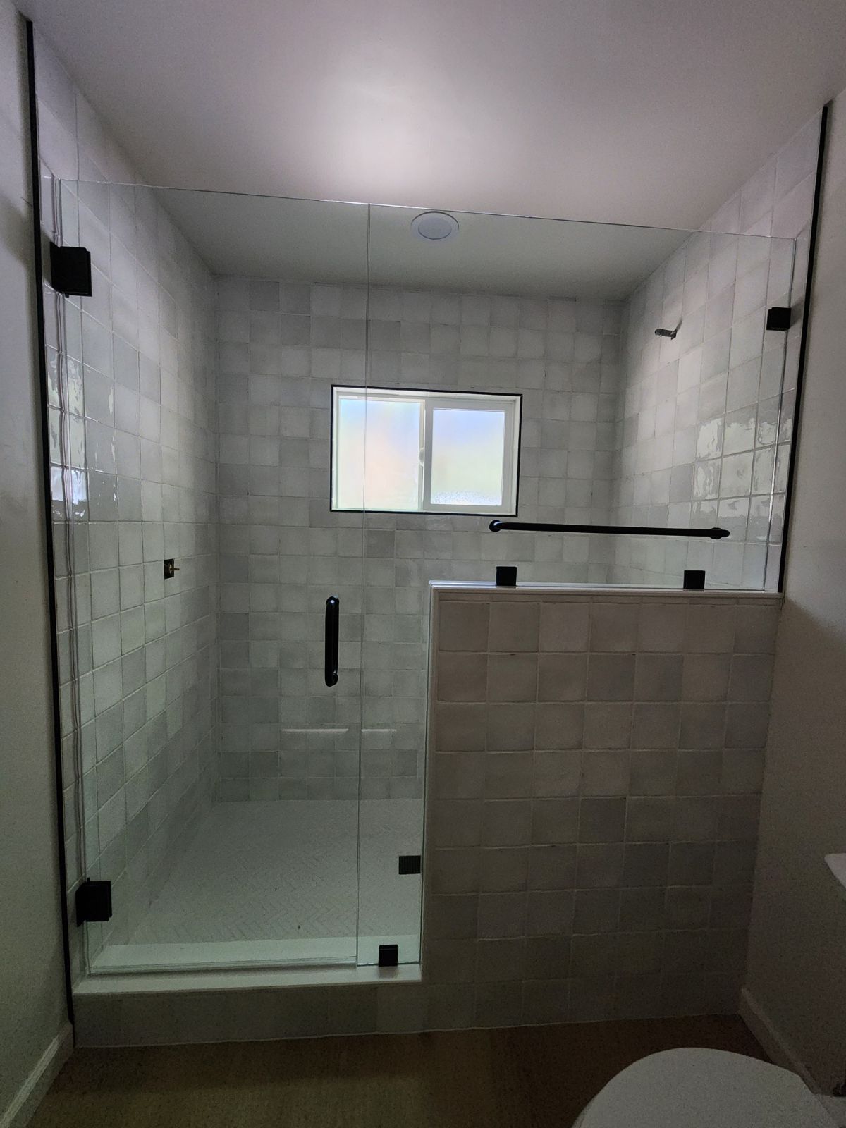 Modern shower stall with glass door, tiled walls, window, and tiled half-wall partition