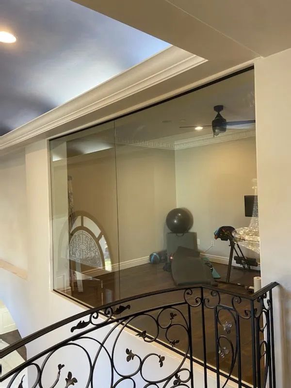 Office seen through an interior glass window, with a desk, chair, ceiling light, and decorative railing in foreground