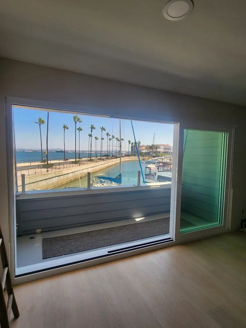 Interior room with open window view of marina, palm trees, and blue water under a bright sky