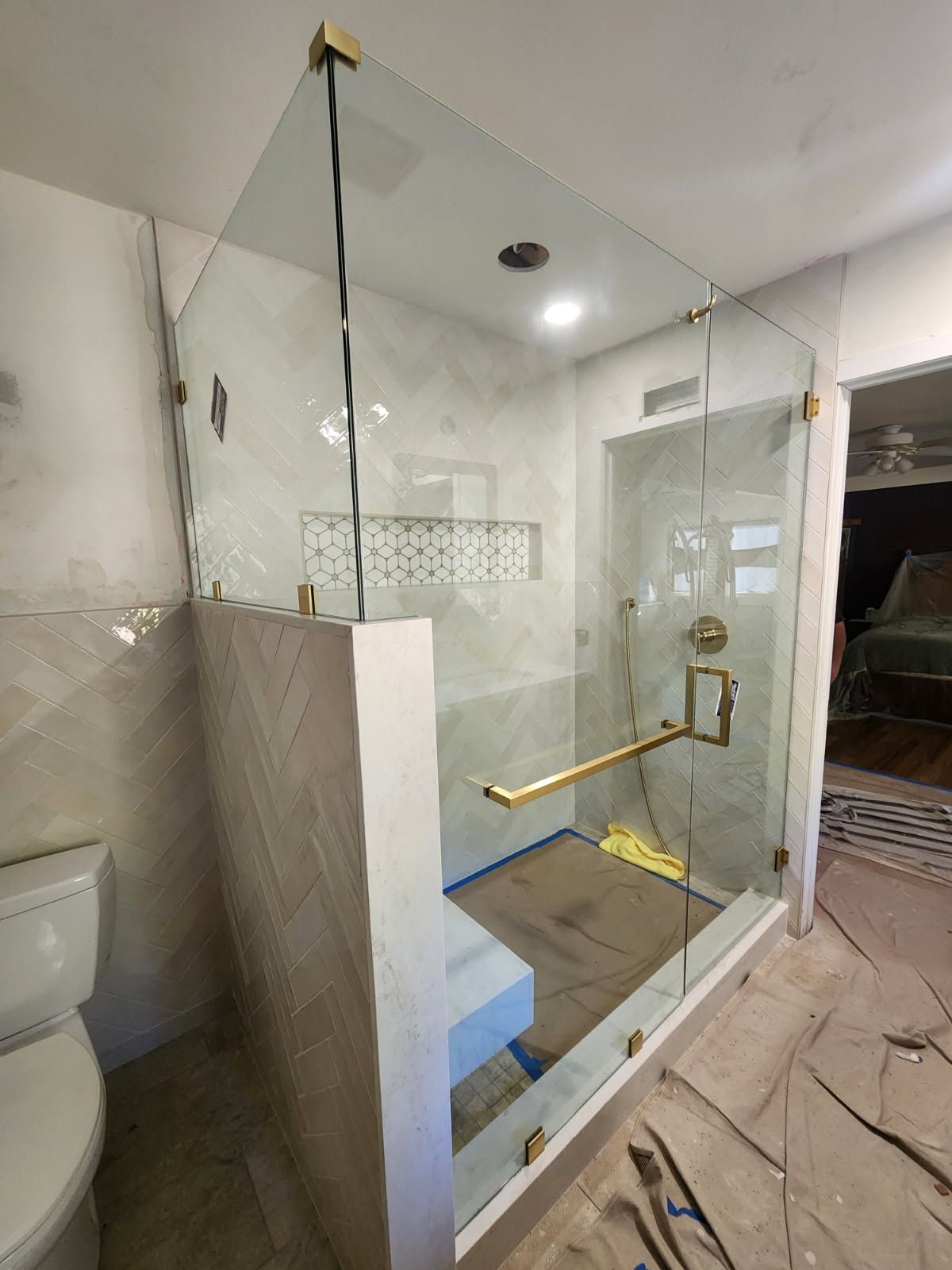 Glass shower stall with brass grab bars and tiled walls in a bathroom