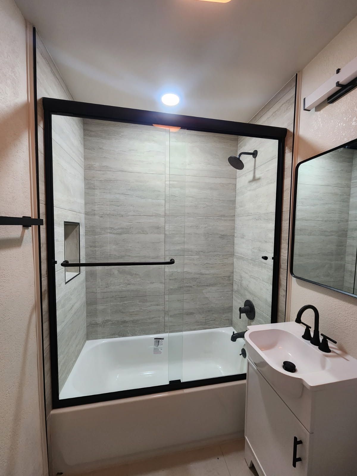 Modern bathroom with glass-enclosed shower-tub and white vanity sink.