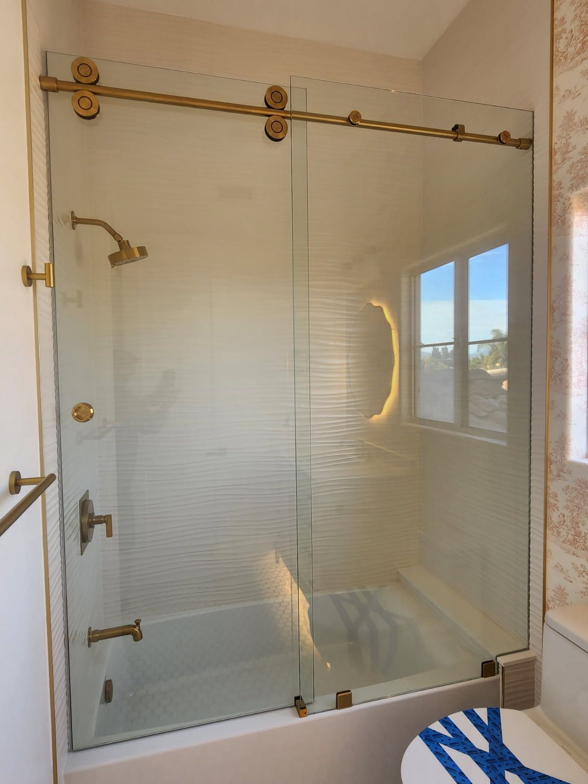 Glass-enclosed walk-in shower with brass fixtures and a window reflection.