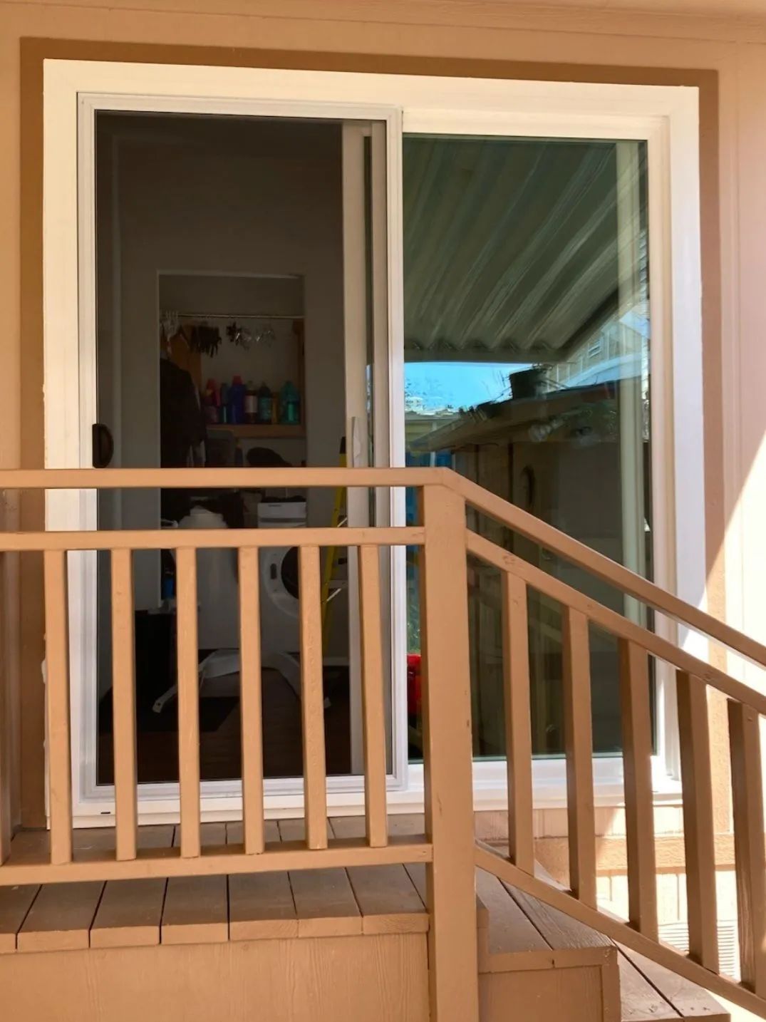 Balcony with wooden railing in front of open sliding glass doors, showing an indoor room and outdoor view.