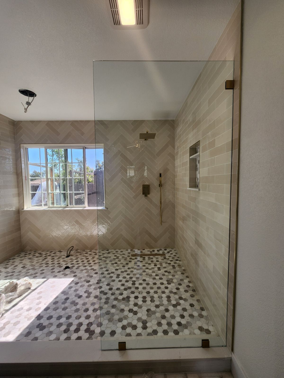Bright modern bathroom with tiled walk-in shower, patterned floor, and window light