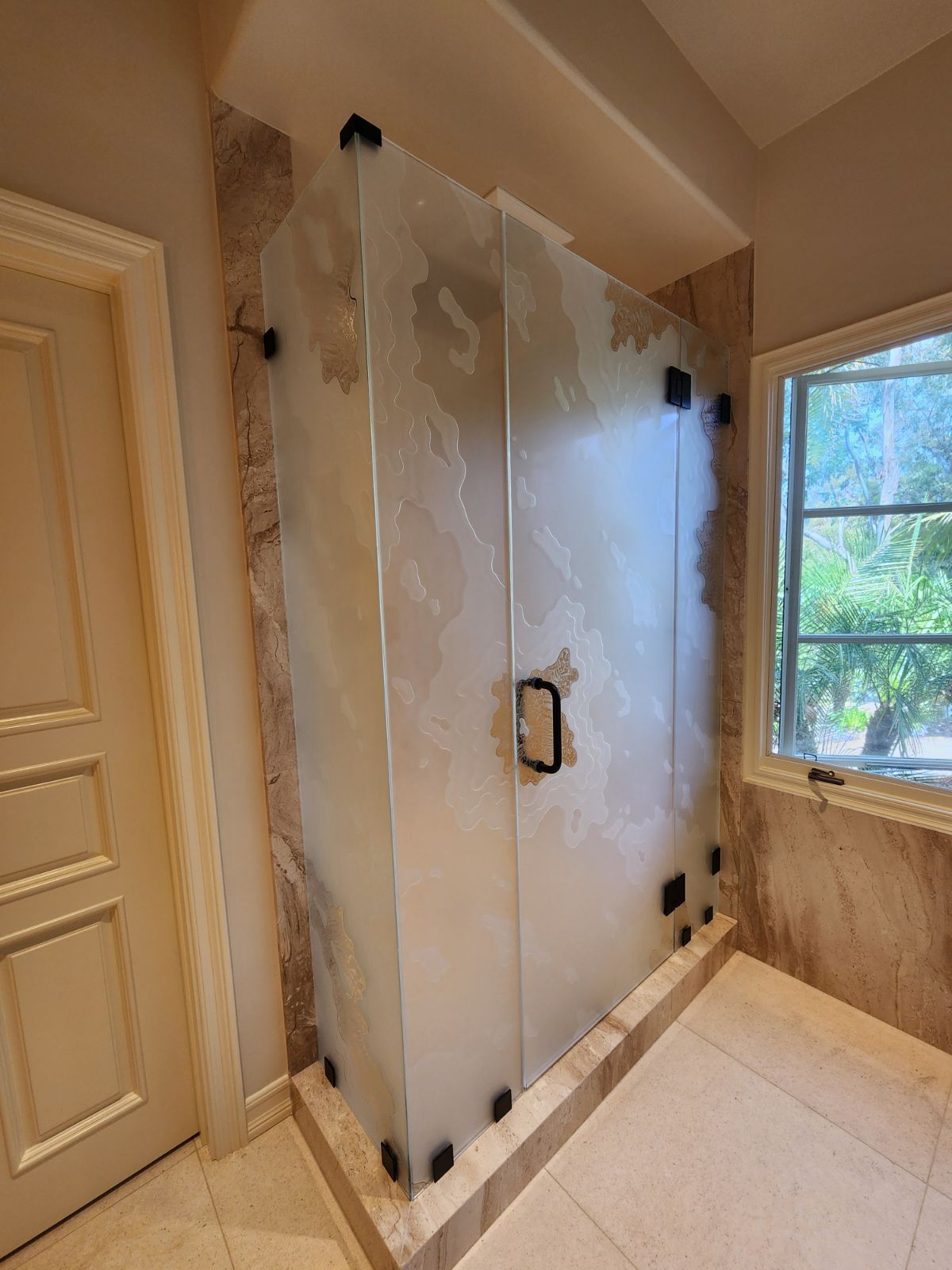 Walk-in shower with frosted glass door and marble tile walls in a bright bathroom