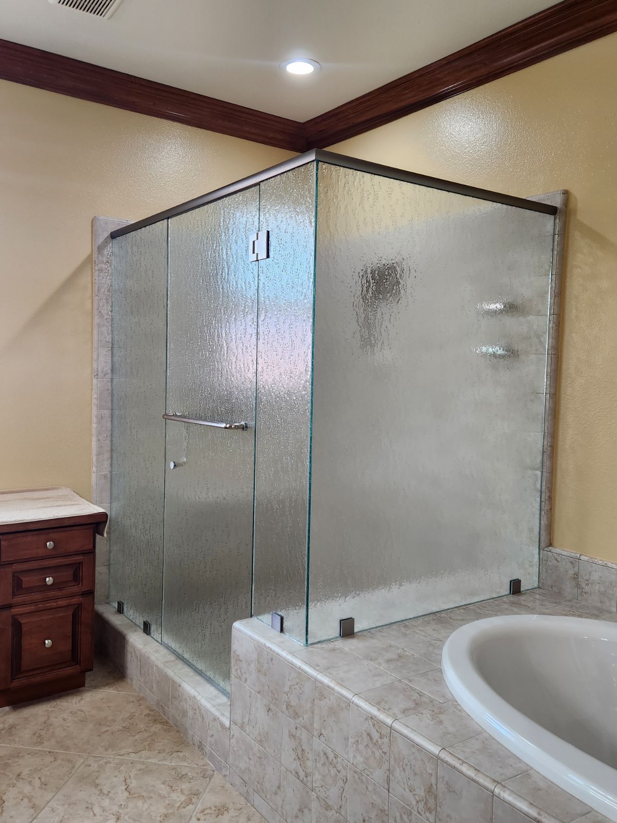 Glass walk-in shower with frosted panels beside a bathtub in a beige bathroom.