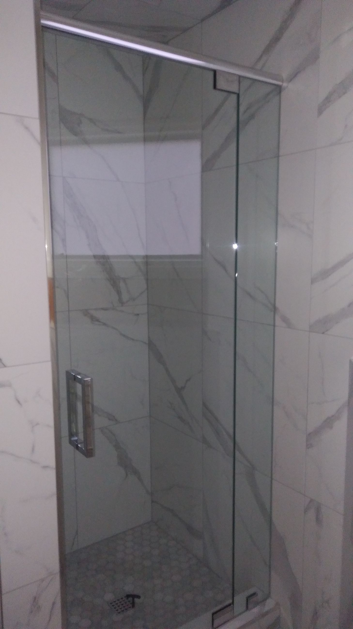 Glass shower enclosure with chrome handle in a gray marble-tiled bathroom