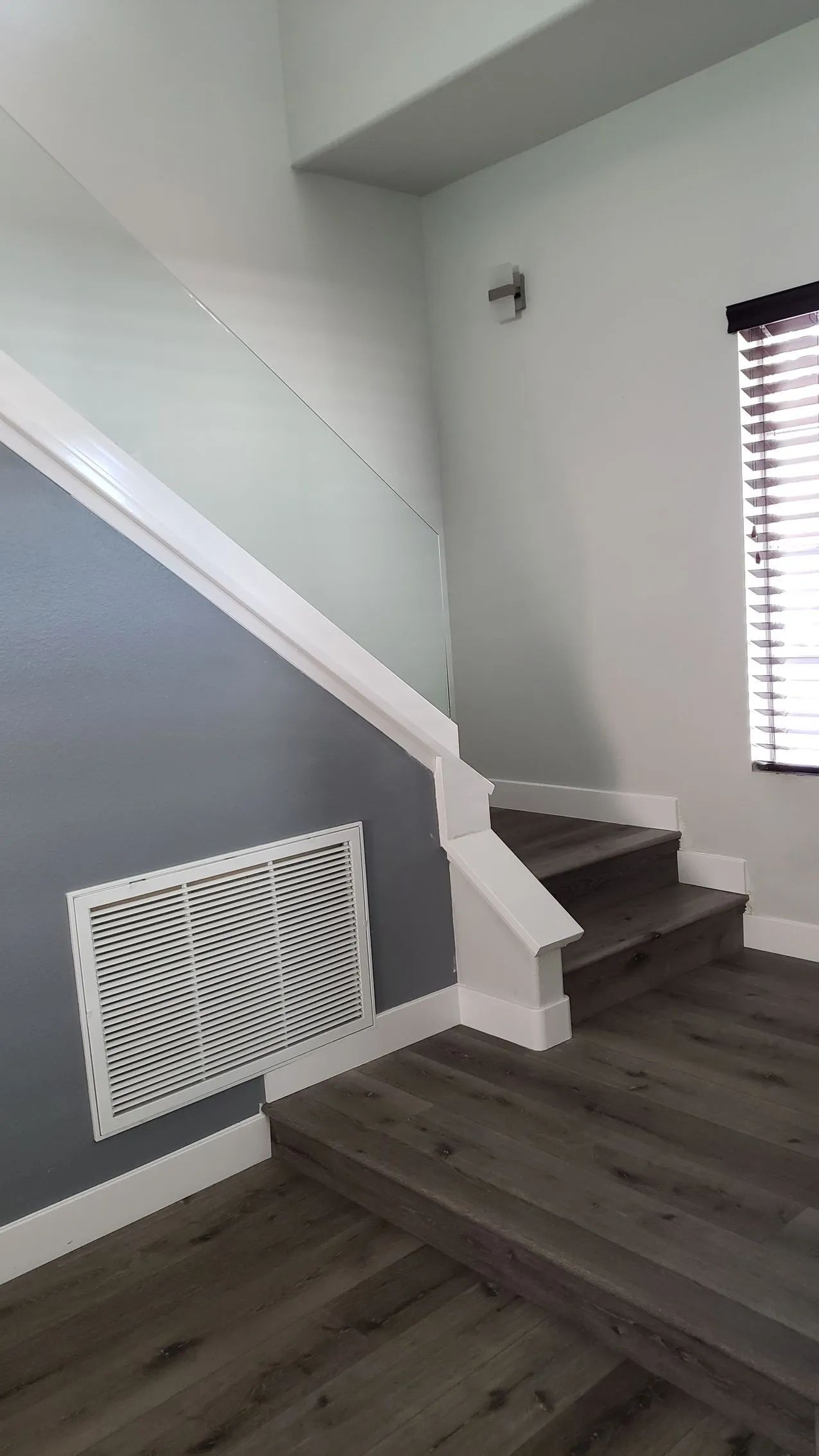Stairway with gray walls, white railing, dark wood steps, a vent, and a window with blinds.