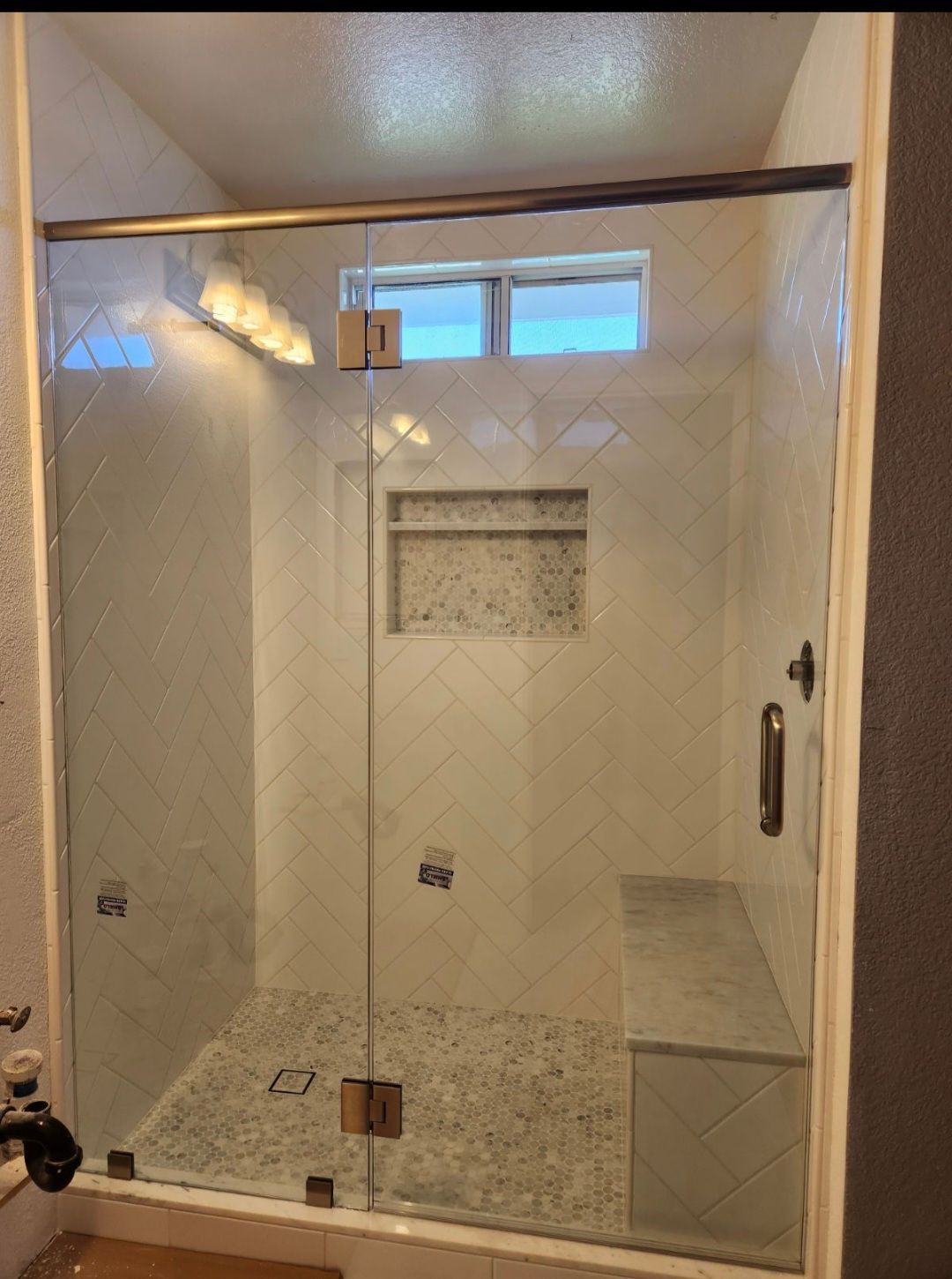 Frameless glass shower stall with beige tile walls, built-in niche, and chrome handle.