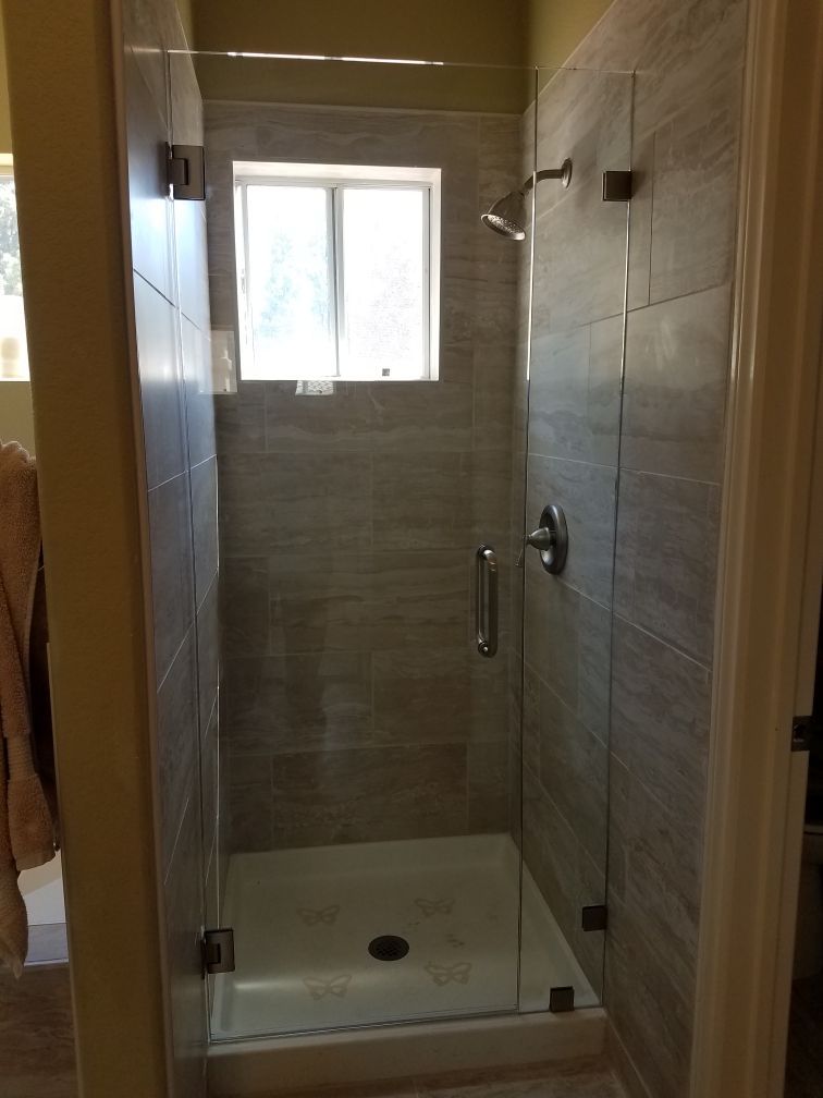 Small tiled shower stall with glass door, window, and built-in shower base in a narrow bathroom.