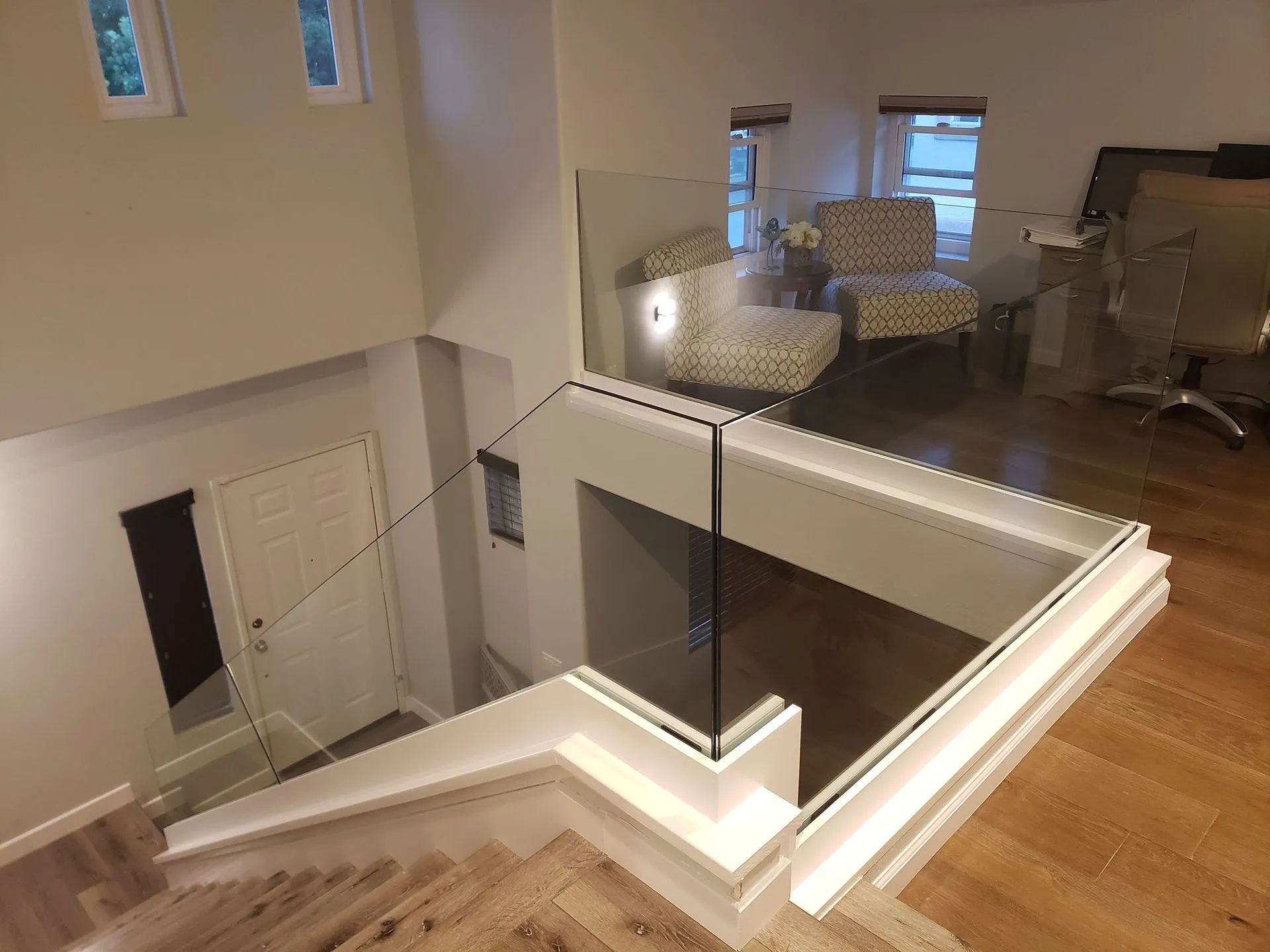 Staircase landing with glass railing overlooking a bright upstairs bedroom and open hallway.