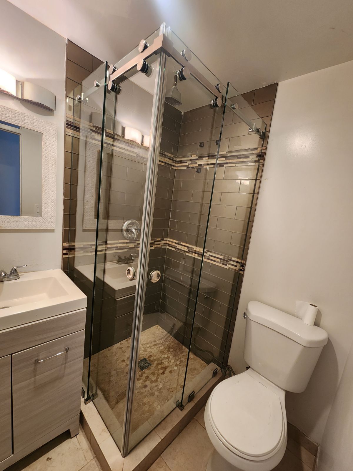 Modern bathroom with glass shower, toilet, and sink vanity; beige tile walls and floor.