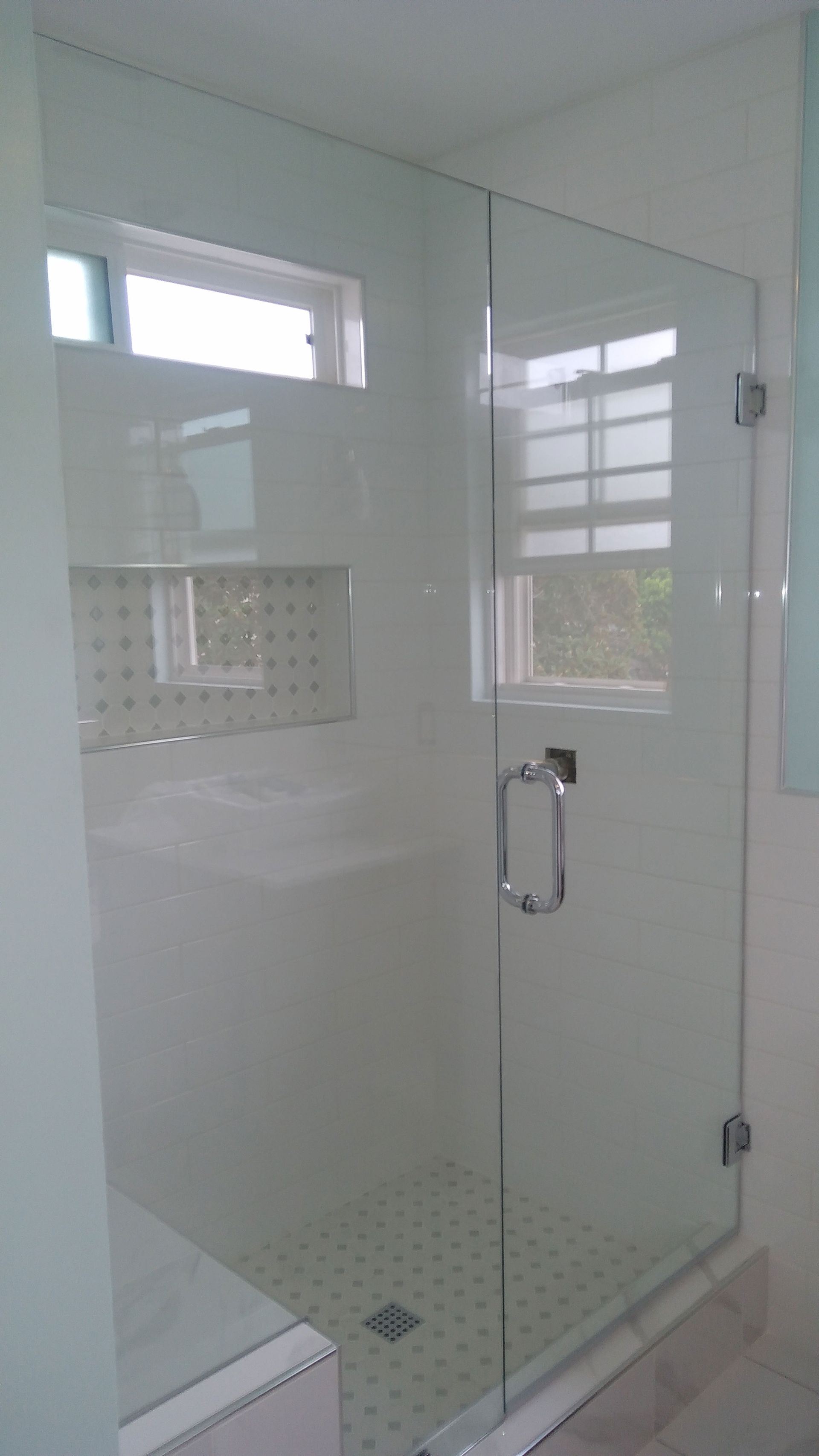 Glass-enclosed white tiled shower with chrome door handle and window light
