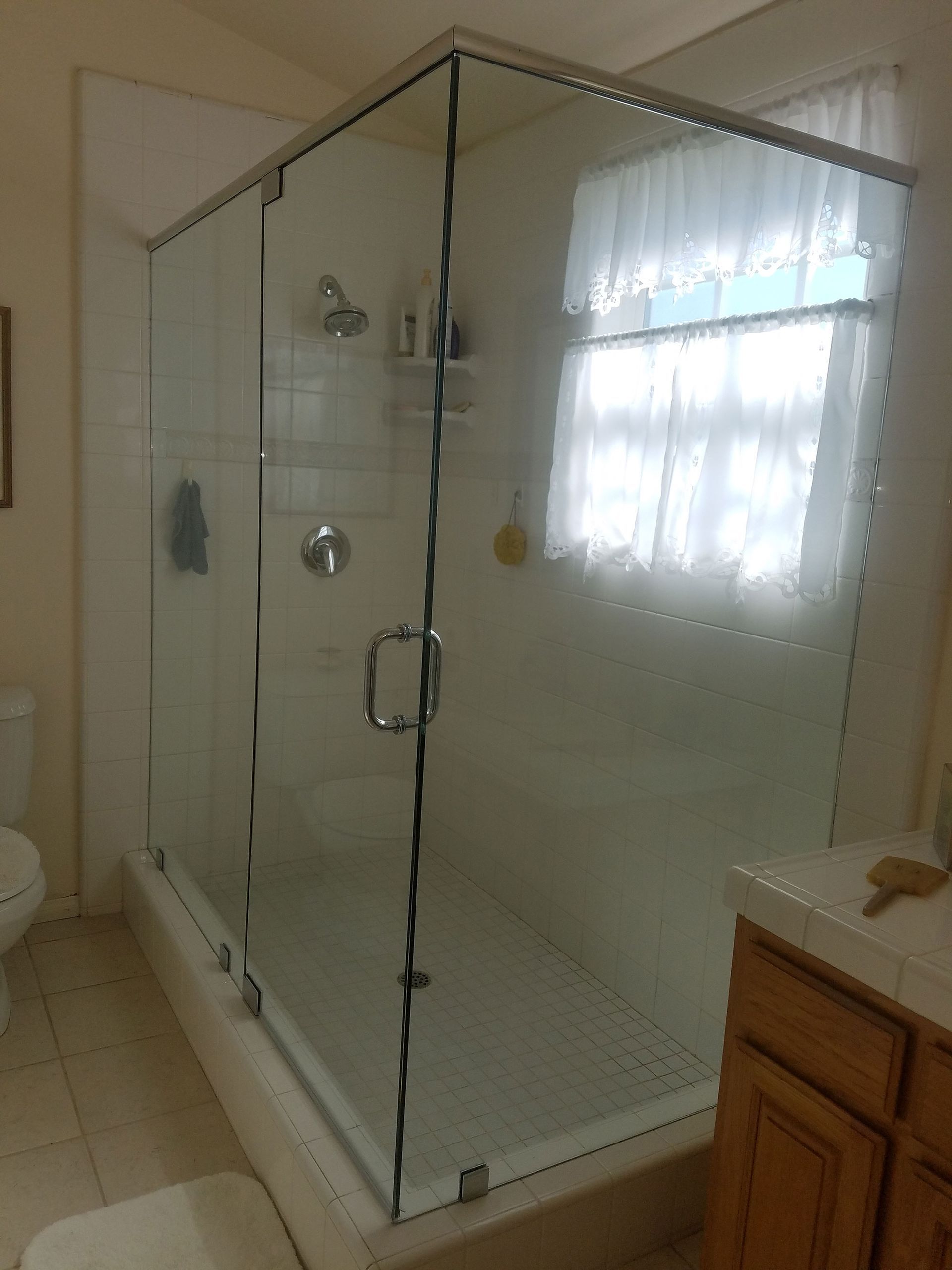 Glass corner shower enclosure in a bathroom with chrome fixtures and a wood vanity nearby