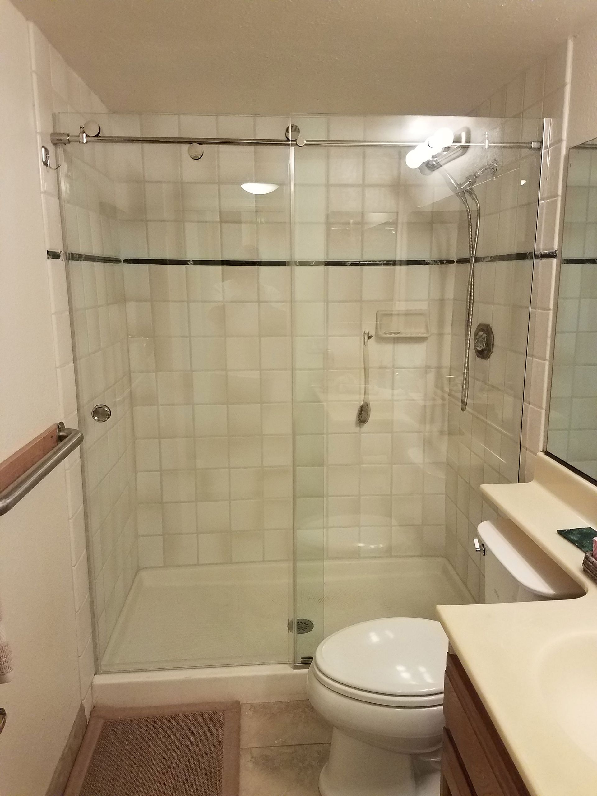 Bathroom with glass-enclosed shower, tiled walls, and a toilet beside a sink counter.