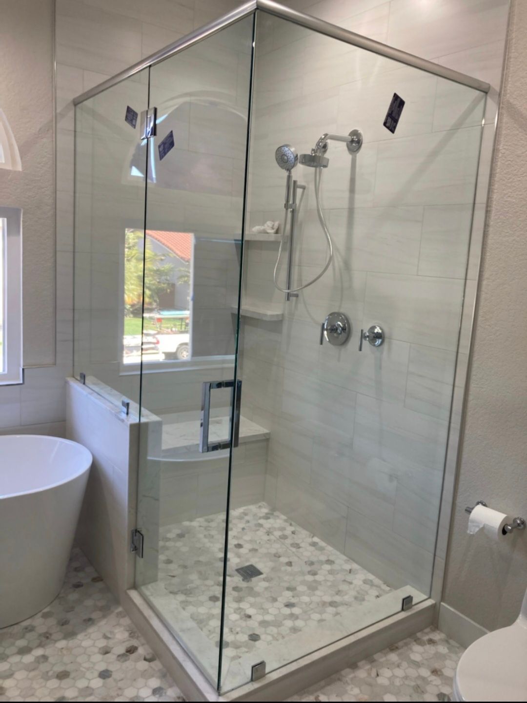 Glass walk-in shower with chrome fixtures and pebble tile floor in a bright bathroom