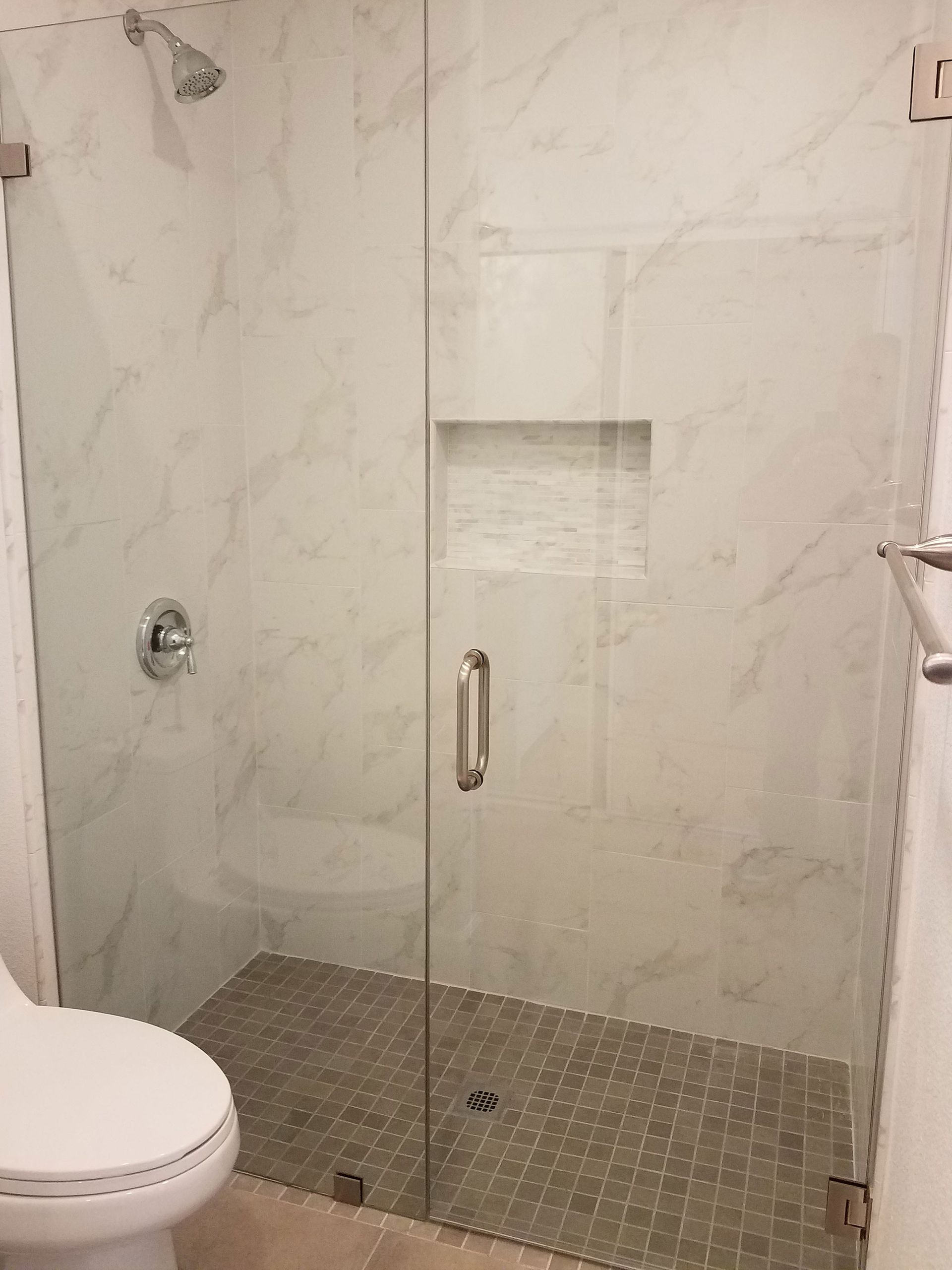 Glass shower stall with chrome handle and marble-pattern walls in a bathroom