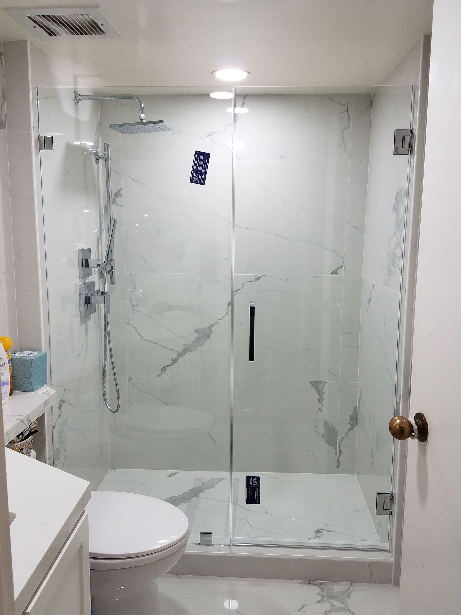 Small bathroom with glass shower enclosure, toilet, and sink vanity in a white tiled space