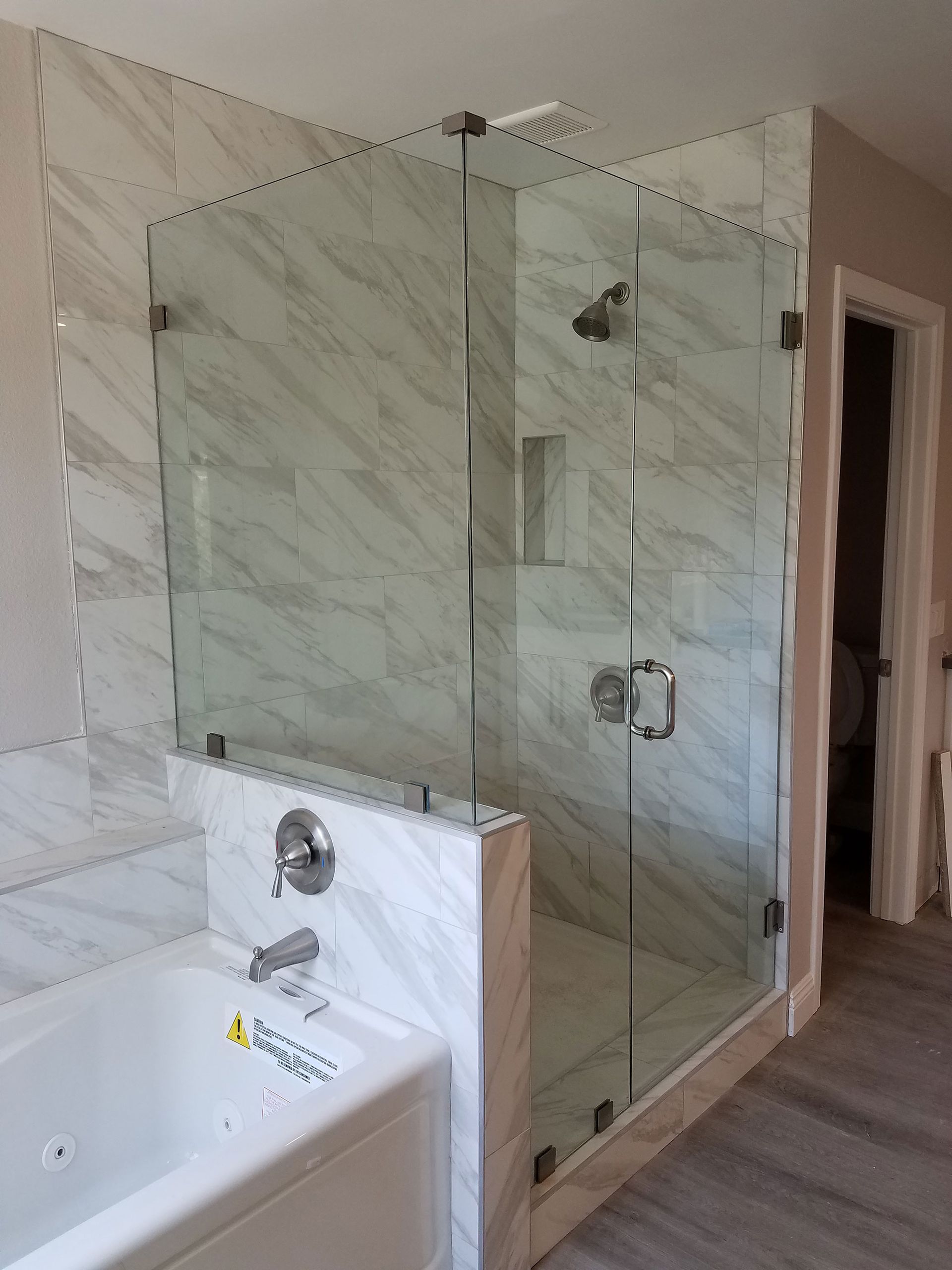 Bathroom with a glass shower enclosure beside a white bathtub and marble tile walls.