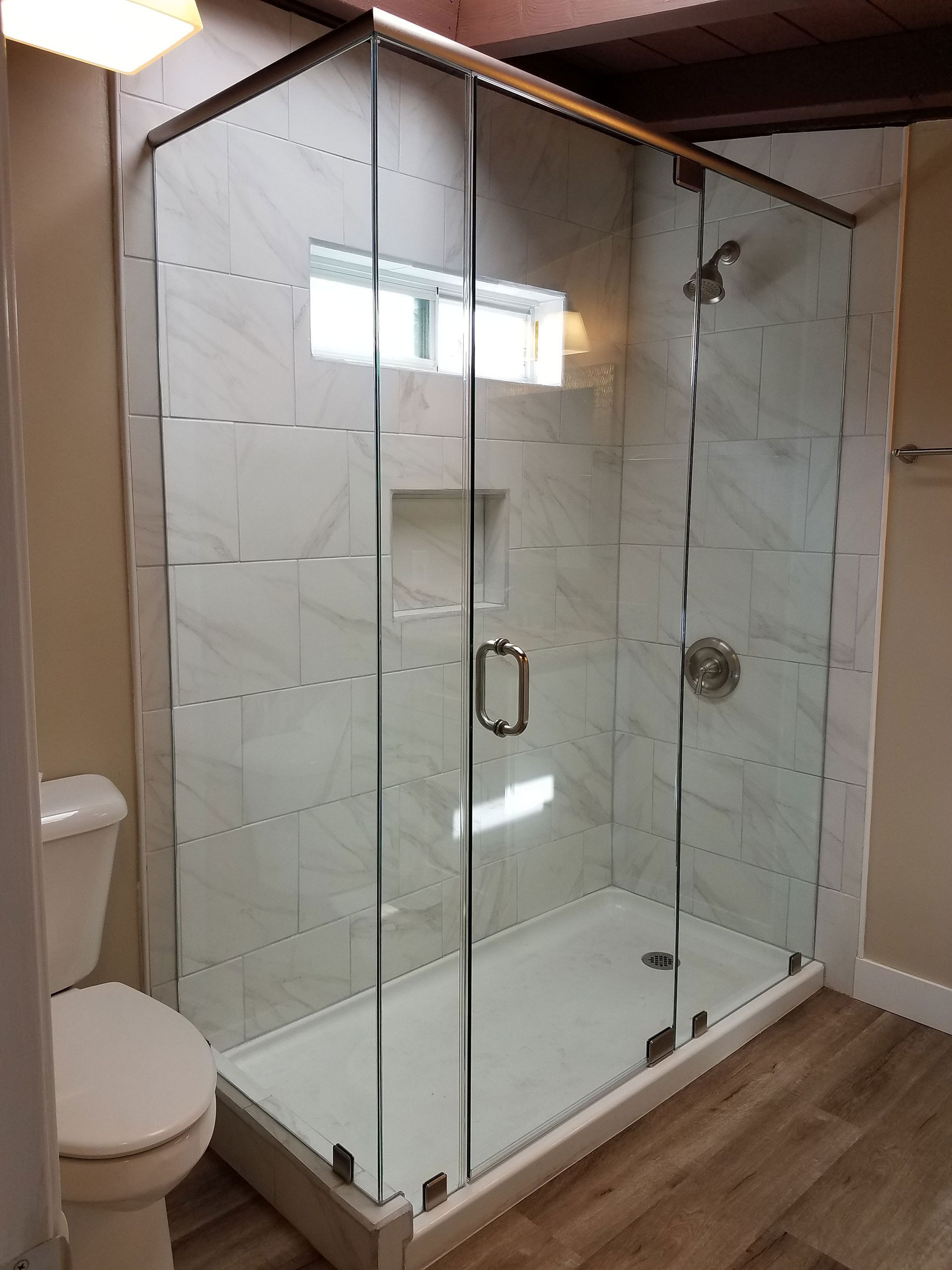 Glass walk-in shower with white tile walls and wood-look flooring in a bathroom.