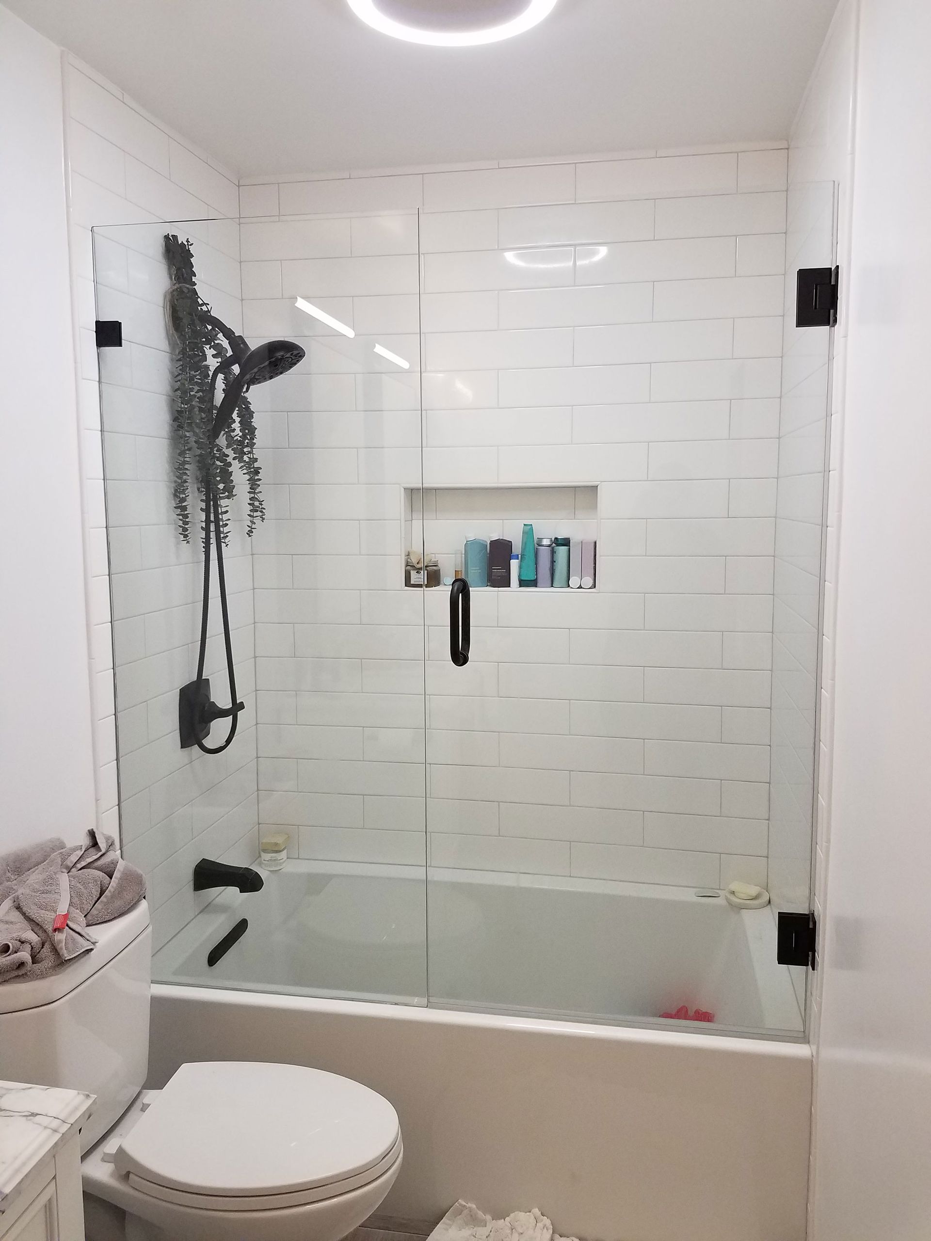 Modern bathroom with glass shower, white tile walls, bathtub, toilet, and ceiling light