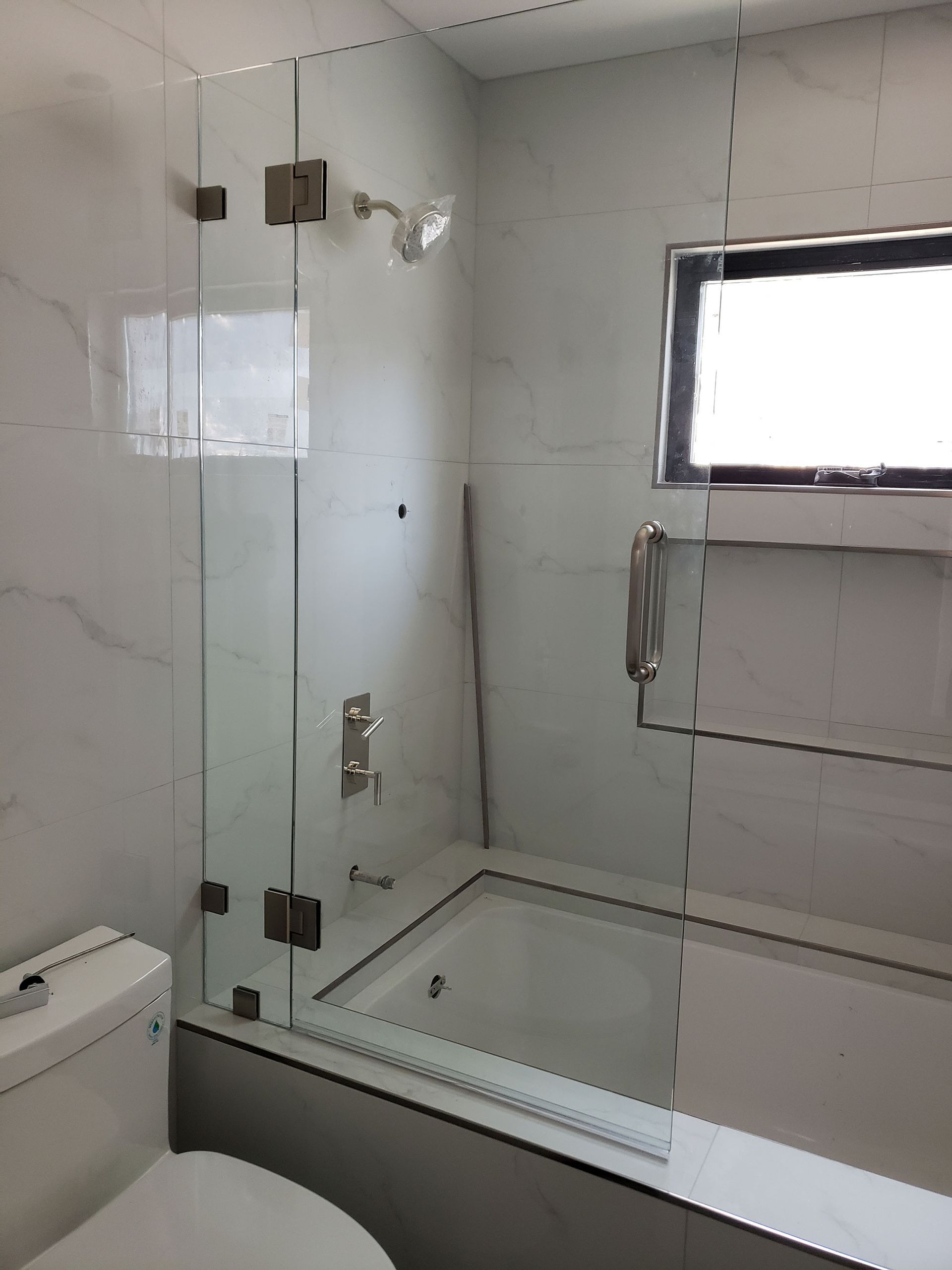 Modern bathroom with glass-enclosed shower, white tile walls, and a window.
