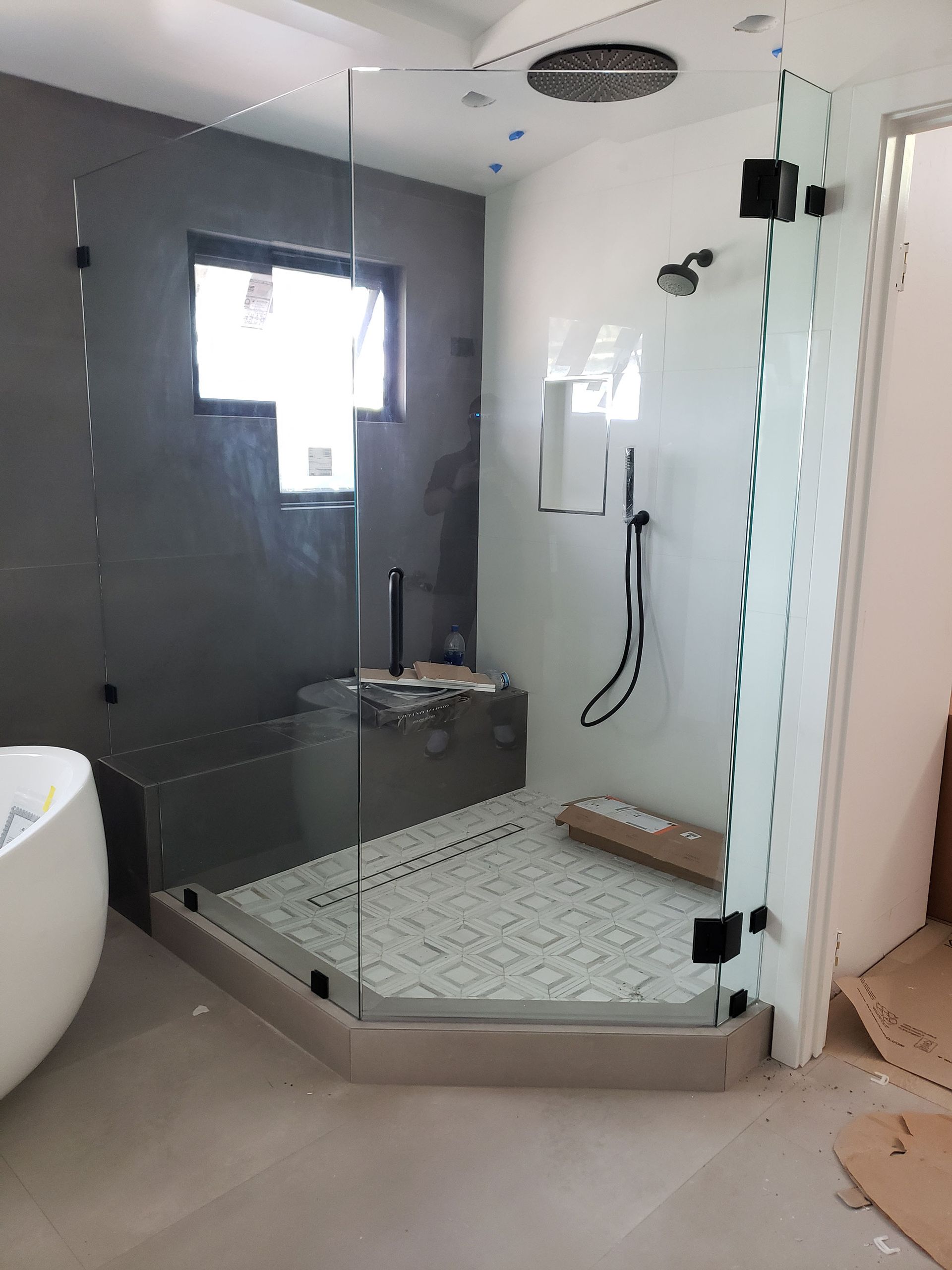 Modern walk-in shower with glass enclosure, gray tile, rain shower head, and white mosaic floor.