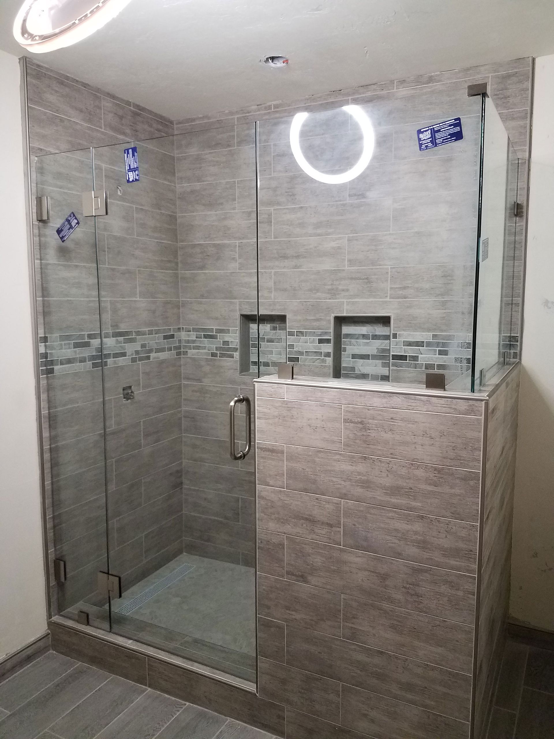 Modern tiled shower enclosure with glass door and partition wall, lit by ceiling light.