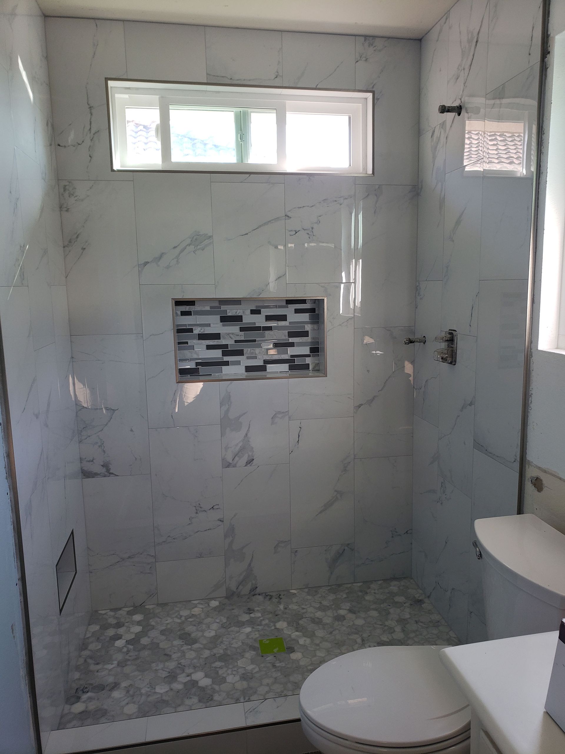 Small tiled bathroom with a walk-in shower, frosted window, and toilet in the foreground.